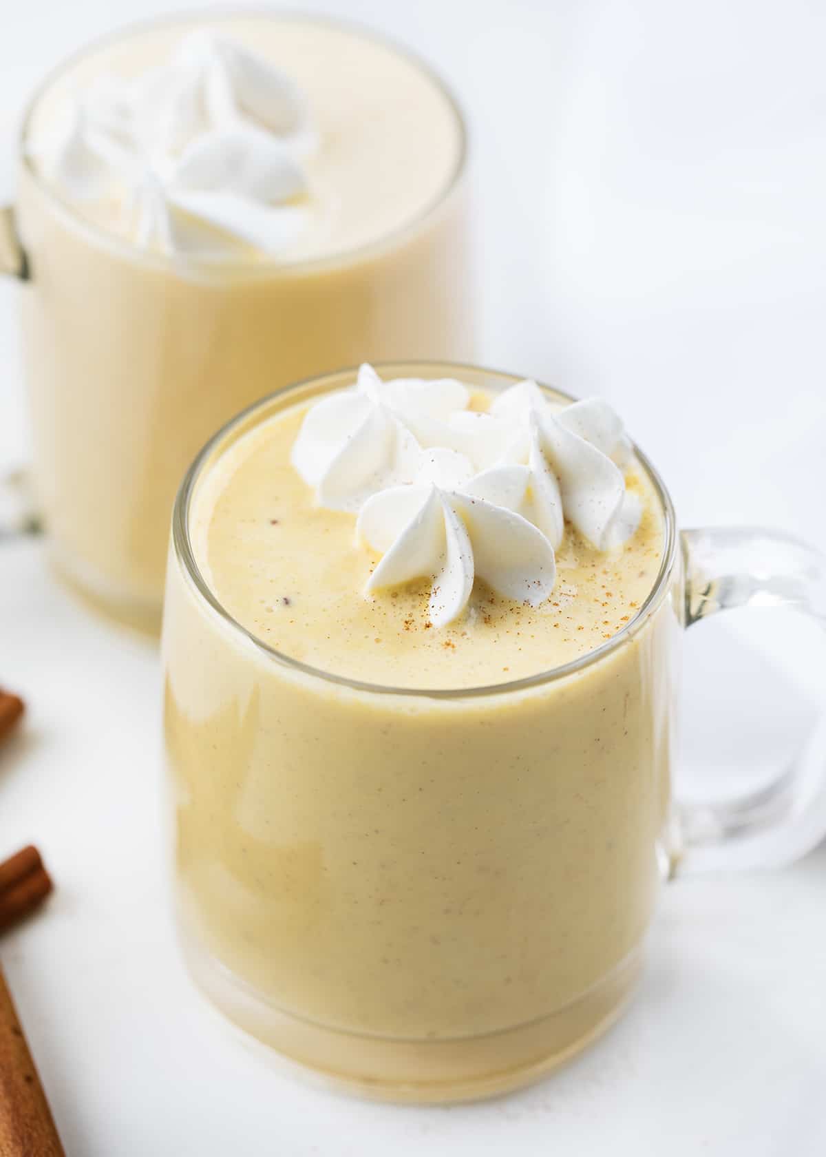 Eggnog is a creamy, egg-yolk-based holiday drink with just the right amount of spice that can be made with or without alcohol. It's delicious either way! And, when you make your own batch, you know exactly what is going into it without all the added preservatives. Better yet, you can adapt the recipe for all ages, making it a Christmas mocktail recipe if you leave out the alcohol. Glass mugs filled with eggnog and topped with whipped cream.