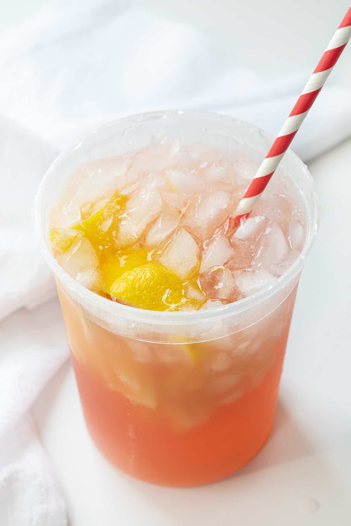 State Fair Strawberry Lemonade is a refreshing and flavorful drink that combines the tartness of lemon with the sweetness of strawberries. It's meant to be one huge extra large drink, intending to last as you wander around a state fair. However, you don't have to mess with any crowds when you can make it at home! State Fair Strawberry Lemonade in a Container on a White Counter.