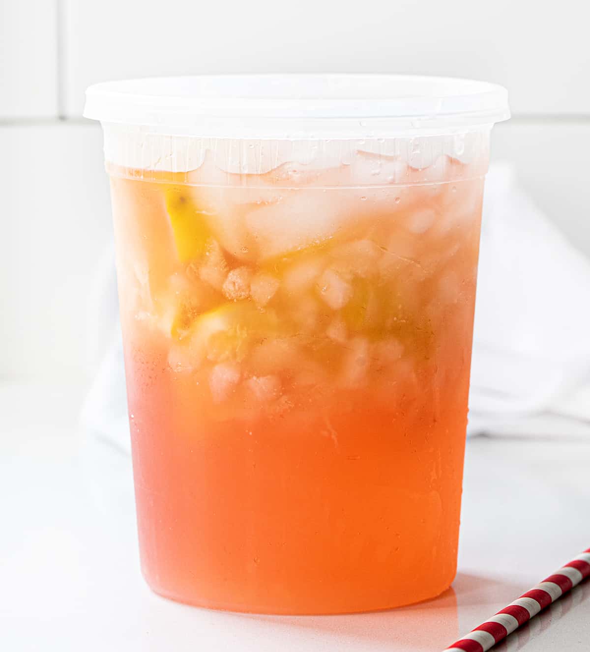 State Fair Strawberry Lemonade is a refreshing and flavorful drink that combines the tartness of lemon with the sweetness of strawberries. It's meant to be one huge extra large drink, intending to last as you wander around a state fair. However, you don't have to mess with any crowds when you can make it at home! State Fair Strawberry Lemonade in a Container on a White Counter.