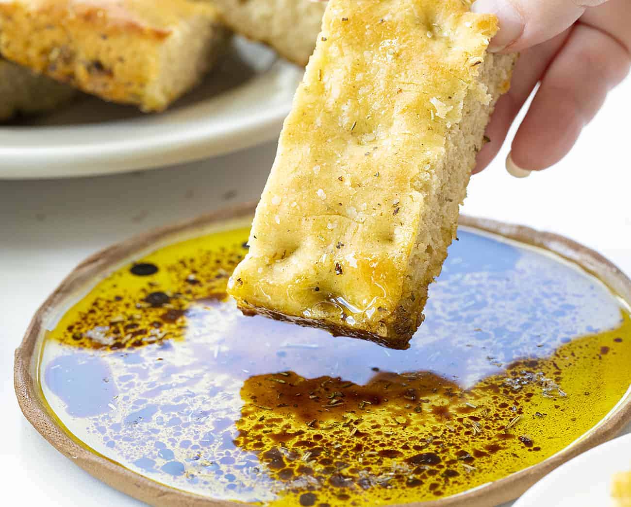 Focaccia Bread is an Italian bread that is made with lots of olive oil and full of Italian seasoning for a delicious and savory snack or appetizer. focaccia bread, bread recipes, Italian bread, i am baker, iambaker, homemade focaccia bread recipe, baking bread Dipping Piece of Focaccia Bread into Oil and Balsamic Vinegar