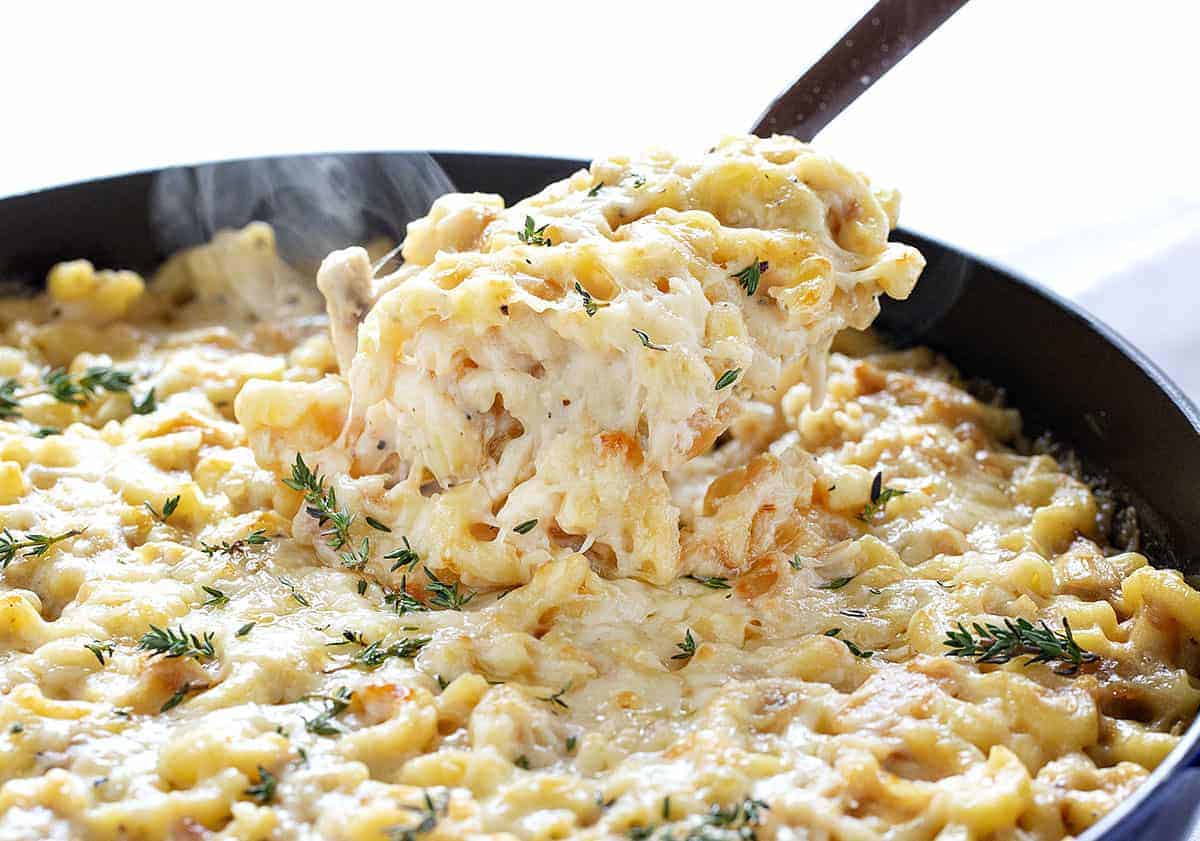 French Onion Chicken Macaroni and Cheese gives you all the flavor of your favorite french onion soup with loads of chicken and cheesy noodles to fill you up! french onion chicken macaroni and cheese, dinner recipes, iambaker, french onion, french onion macaroni and cheese, macaroni and cheese Taking a Scoop of French Onion Chicken Macaroni and Cheese Out of a Skillet
