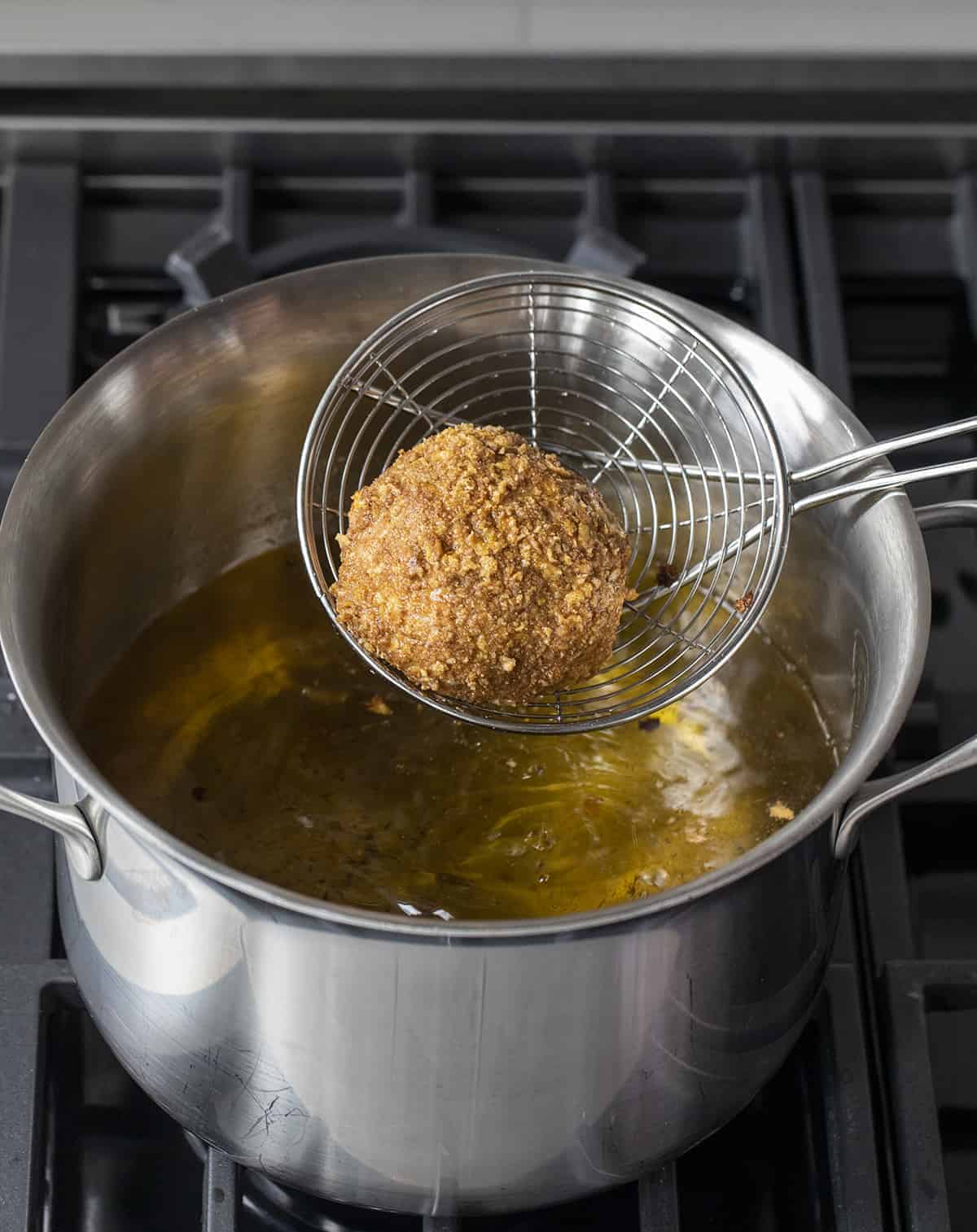 Fried Ice Cream is a frozen ball of ice cream, coated in egg whites, vanilla wafers, cornflakes, and cinnamon, deep-fried to a golden brown. Dessert, No Bake Dessert, Hot Dessert, Ice Cream, Ice Cream Dessert, Summer Desserts, recipes, air fryer fried ice cream, i am baker, iambaker Dipping Fried Ice Cream into Hot Oil and then Removing It.