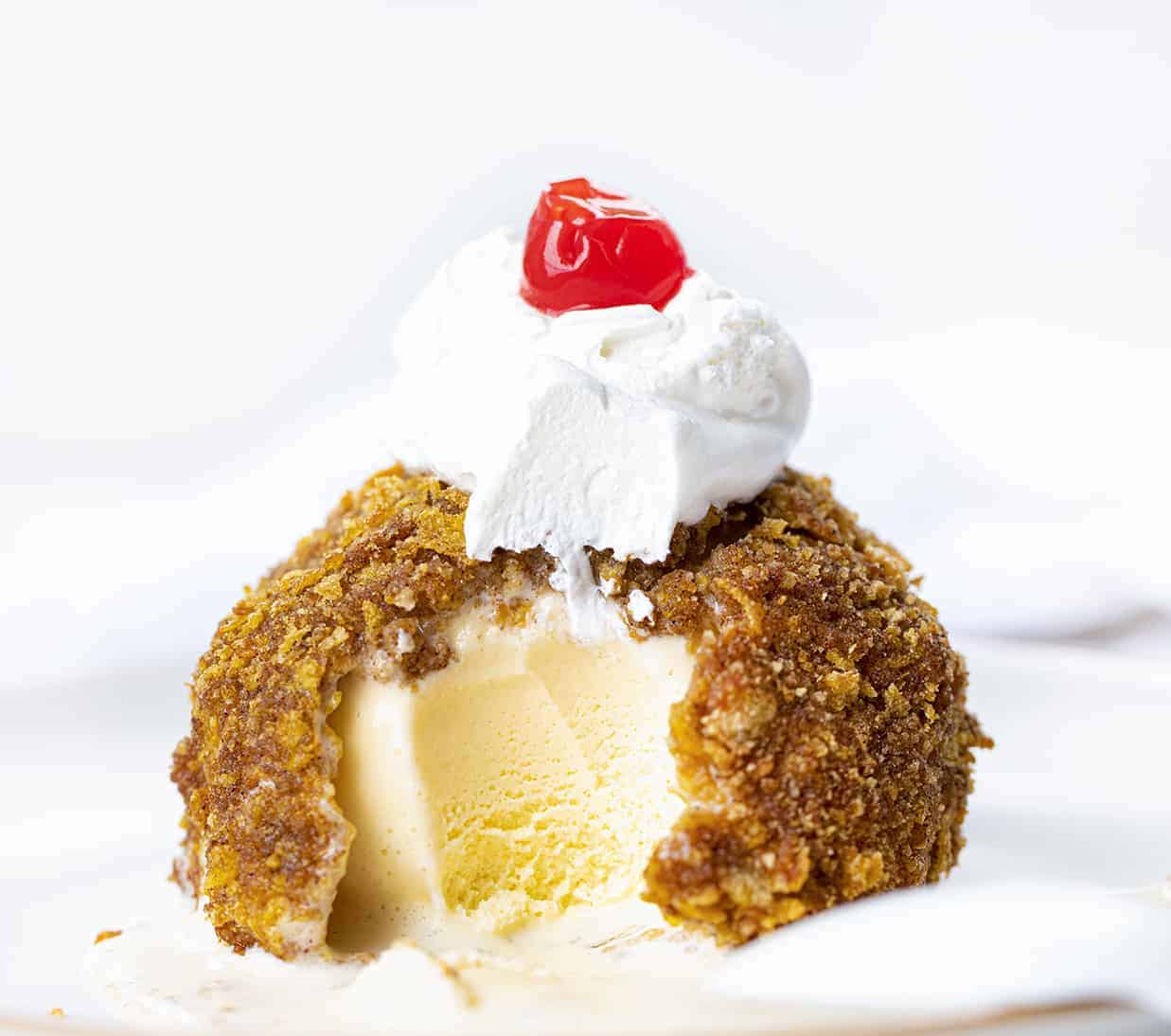 Fried Ice Cream is a frozen ball of ice cream, coated in egg whites, vanilla wafers, cornflakes, and cinnamon, deep-fried to a golden brown. Dessert, No Bake Dessert, Hot Dessert, Ice Cream, Ice Cream Dessert, Summer Desserts, recipes, air fryer fried ice cream, i am baker, iambaker Fried Ice Cream with Bite Take out on a White Plate.