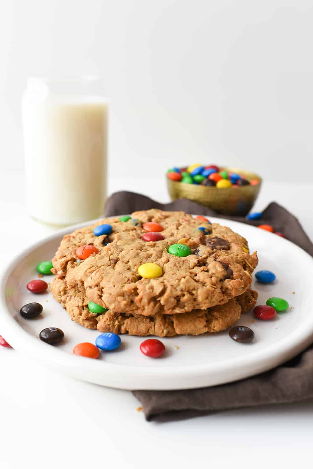 This classic recipe is kicked up a notch and made GIANT! Peanut butter and M&M's work together to create the best cookie recipe ever! #monstercookies #cookies #cookierecipe #iambaker Monster Cookies on White Plate