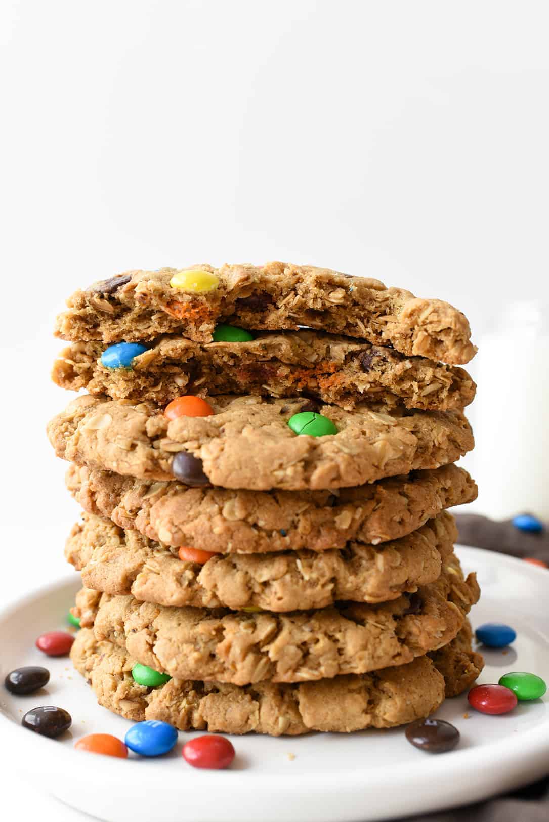 This classic recipe is kicked up a notch and made GIANT! Peanut butter and M&M's work together to create the best cookie recipe ever! #monstercookies #cookies #cookierecipe #iambaker Monster Cookie Recipe Stacked and Top Cookie Broken in Half