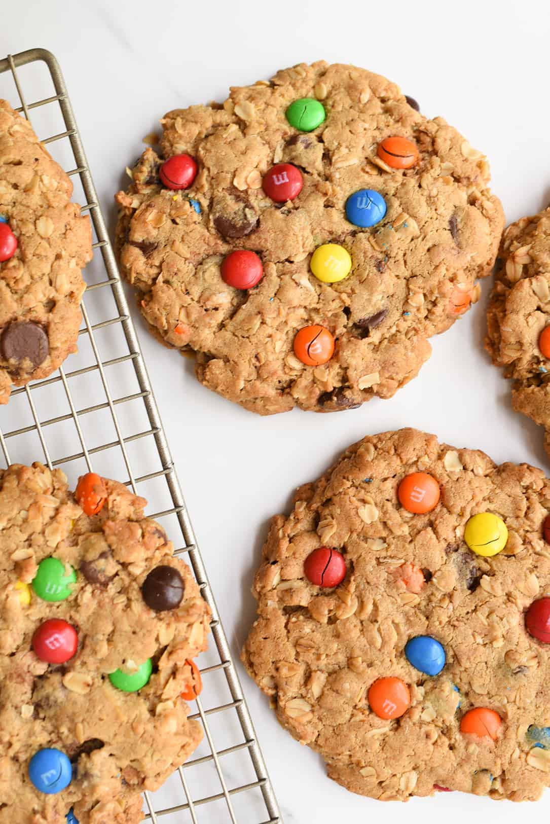 This classic recipe is kicked up a notch and made GIANT! Peanut butter and M&M's work together to create the best cookie recipe ever! #monstercookies #cookies #cookierecipe #iambaker Giant Monster Cookie Recipe On Cooling Rack