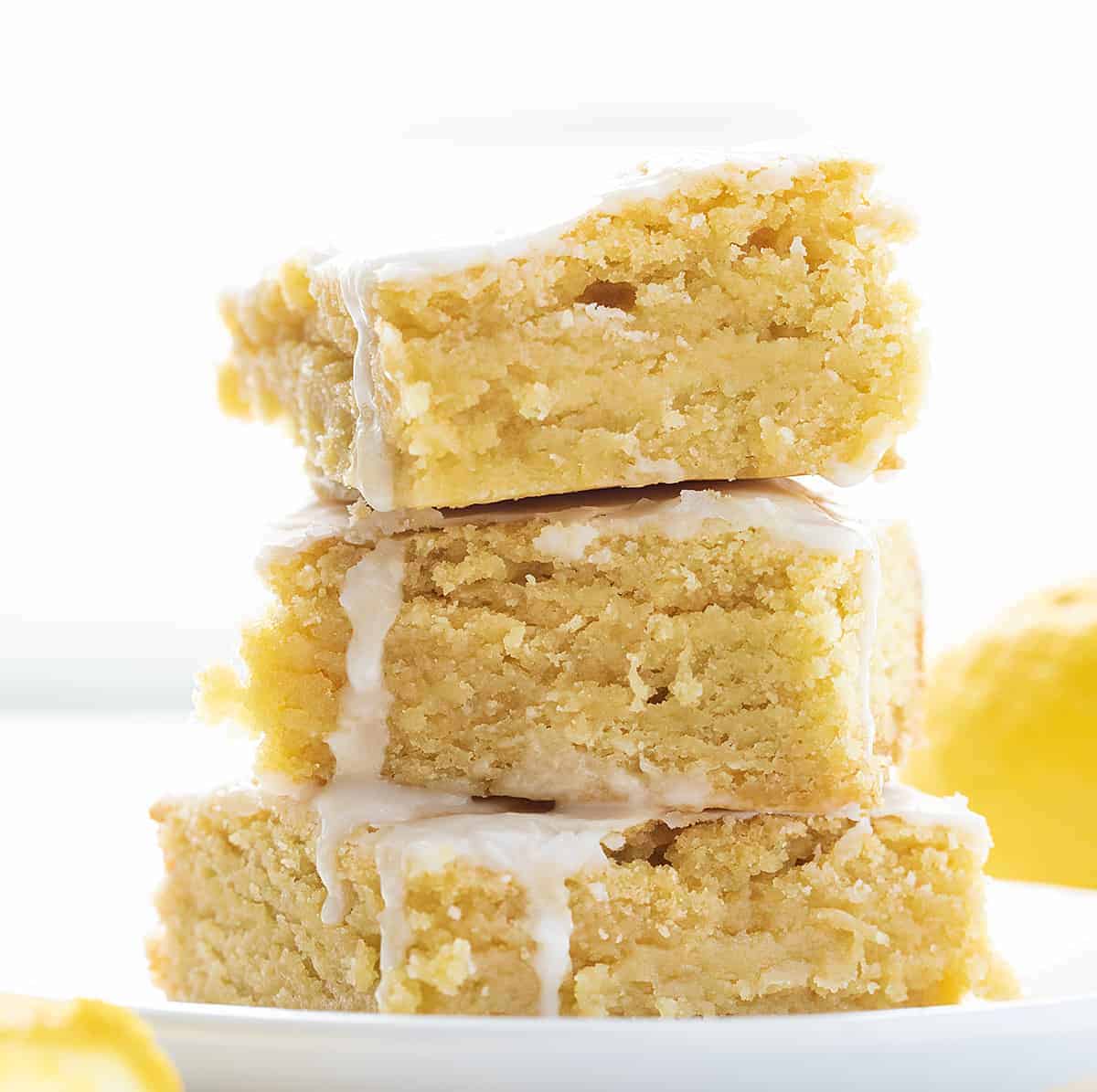 Lemon Brownies are dessert bars that are dense and moist with a lemony flavor and topped with a vanilla glaze. Lemon Brownies, Lemon Blondies, Fudgy Lemon Brownie, The Best Lemon Brownie, Baking, Lemon Recipes, Dessert, i am baker, iambaker Stack of Lemon Brownies on Plate