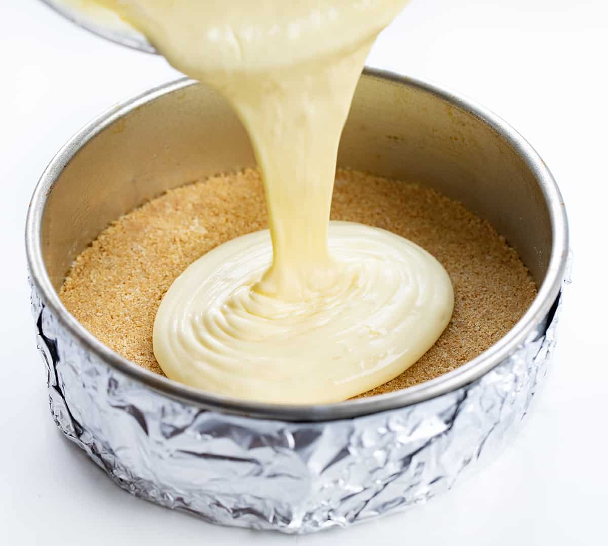 Lemon Cheesecake is a graham cracker crust filled with a light and smooth lemon-flavored filling, all topped with a creamy sour cream layer. If you appreciate the vibrant and refreshing taste of lemons and love cheesecake, this will be your new favorite dessert! Pouring Lemon Cheesecake Batter into a Pan with Graham Cracker Crust.