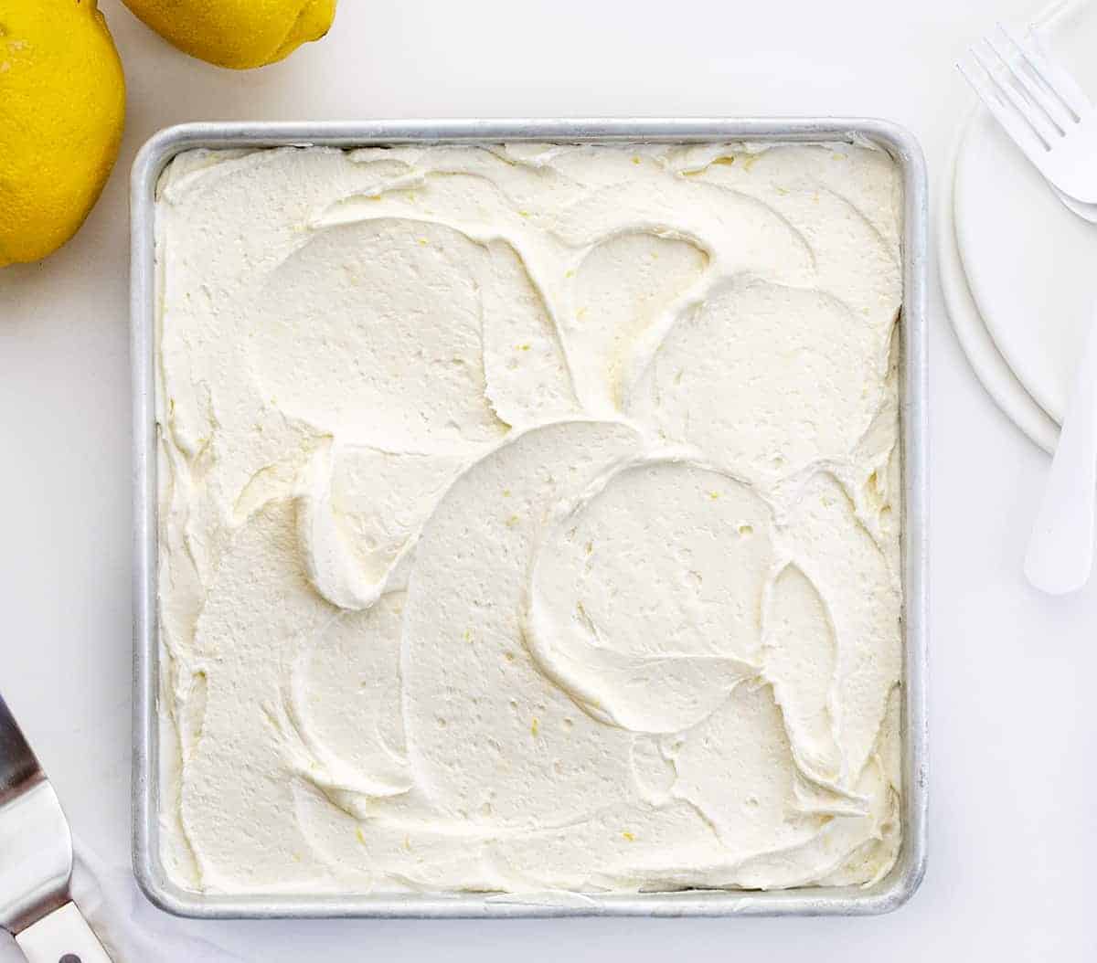 Lemon Crazy Cake is a cake made without milk, eggs, or butter, but full of lemon flavor with a light and fluffy lemon buttercream on top. Lemon Depression Cake, Lemon Wacky Cake, Crazy Cake, Wacky Cake, Depression Cake, Cake with No Milk, Lemon Cake with No Eggs, Lemon Cake with No Butter, Dairy Free Lemon Cake, Desserts, Baking, Summer time desserts, lemon buttercream, recipes, i am baker, iambaker Pan of Lemon Crazy Cake with Lemon Buttercream Frosting in Swirls from Overhead.