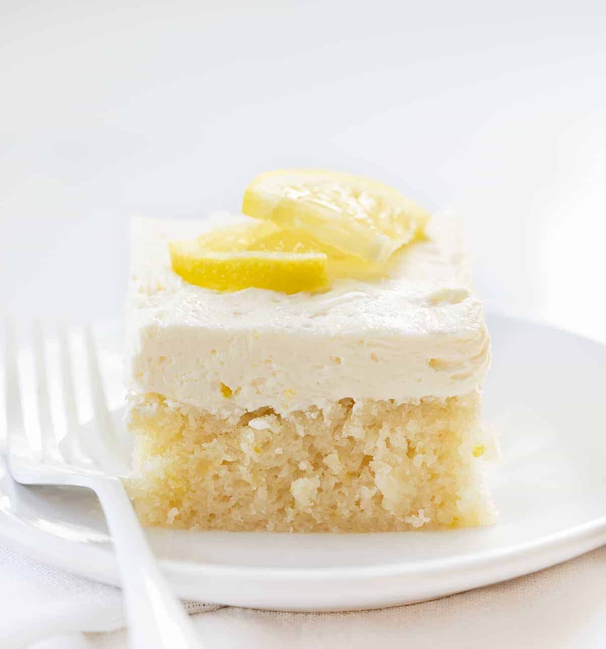 Lemon Crazy Cake is a cake made without milk, eggs, or butter, but full of lemon flavor with a light and fluffy lemon buttercream on top. Lemon Depression Cake, Lemon Wacky Cake, Crazy Cake, Wacky Cake, Depression Cake, Cake with No Milk, Lemon Cake with No Eggs, Lemon Cake with No Butter, Dairy Free Lemon Cake, Desserts, Baking, Summer time desserts, lemon buttercream, recipes, i am baker, iambaker One Piece of Lemon Crazy Cake on a White Plate with White Fork.