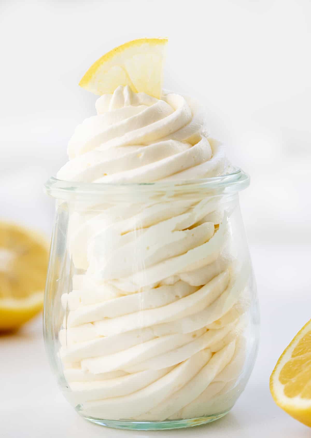 Lemon Ermine Frosting is a smooth, creamy, and buttery frosting made with a cooked lemon juice and flour mixture for just the right lemony zing in every taste. It has a smooth-as-silk texture and a POP of bright lemon tartness that pairs so well with the subtle sweetness of classic ermine frosting. It will give many baked goods a bright lemon flavor! It is perfect for piping and frosting cakes! Lemon Ermine Frosting Piped into a Glass Jar with Lemons around it.