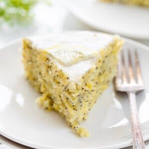 Piece of Lemon Poppy Seed Cake on a White Plate with Green Babysbreath in the Background.