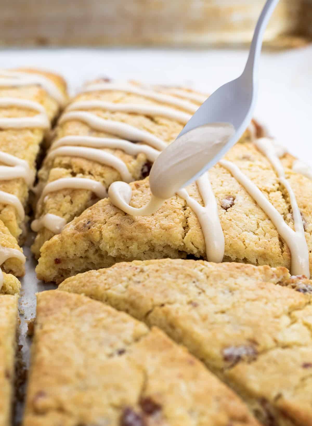 This Maple Bacon Scones recipe is a unique twist on a classic breakfast treat, featuring the perfect blend of sweet maple syrup and salty bacon. The scone has a tender inside and crispy top and is finished with a delicious maple glaze and crumbled bacon. This recipe is easy to follow and uses common ingredients, so don't be intimidated by the thought of making scones! Drizzling Maple Glaze over Maple Bacon Scones.