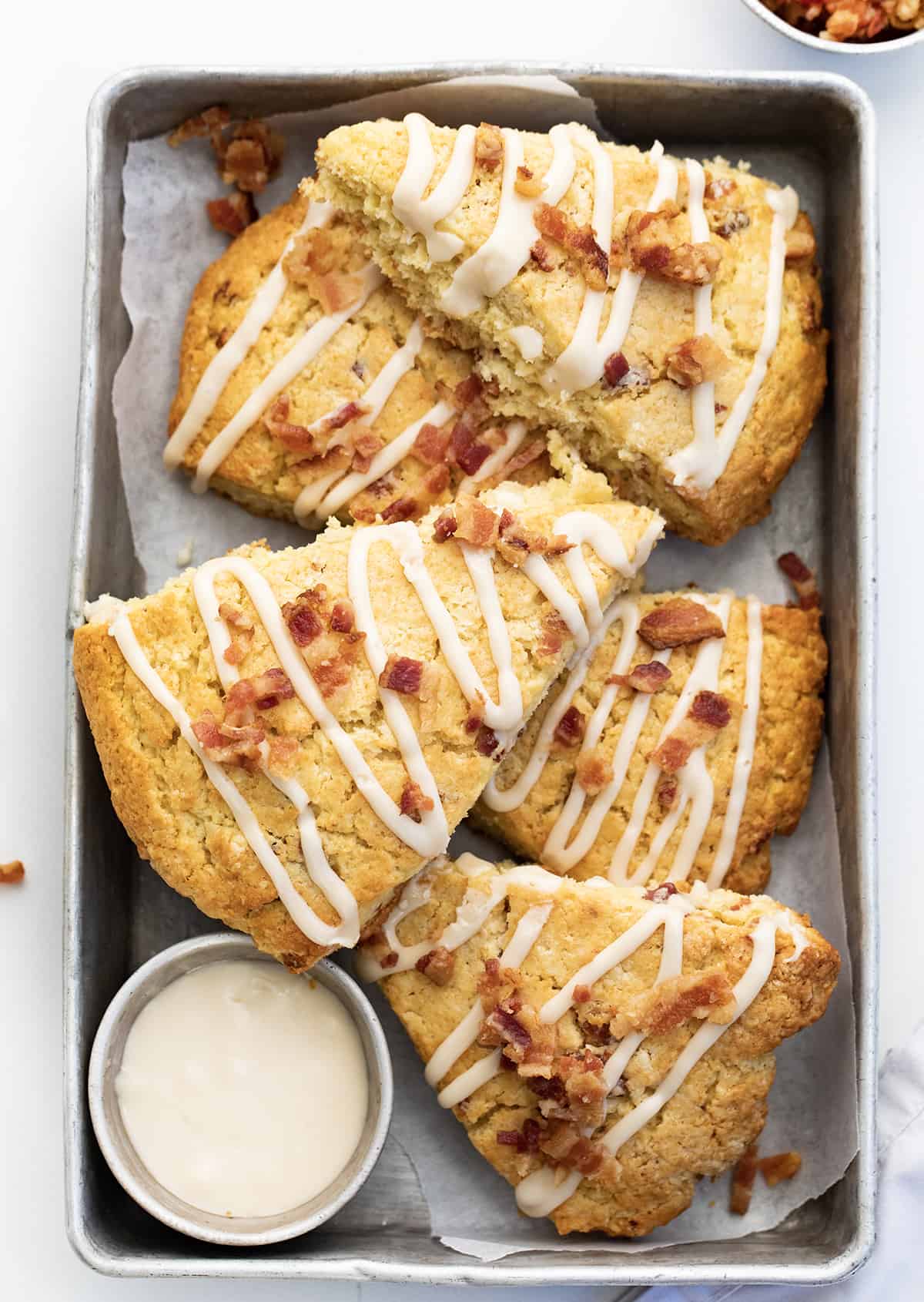 This Maple Bacon Scones recipe is a unique twist on a classic breakfast treat, featuring the perfect blend of sweet maple syrup and salty bacon. The scone has a tender inside and crispy top and is finished with a delicious maple glaze and crumbled bacon. This recipe is easy to follow and uses common ingredients, so don't be intimidated by the thought of making scones! Pan of Maple Bacon Scones with Extra Maple Glaze.