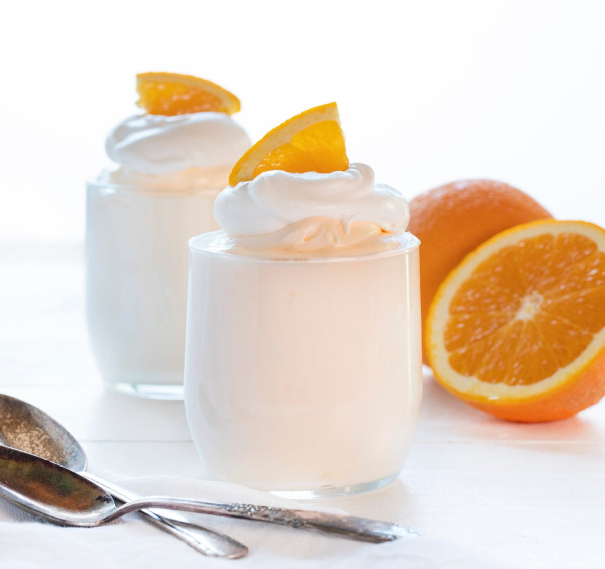 The best no-bake desserts to get your sweet tooth through the summer! no bake, no bake desserts, desserts, recipes, cheesecake, cookies, bars, cake, pudding, mousse, puppy chow, muddie buddies, rice krispy bars, dessert, memorial day dessert, labor day desserts, i am baker, iambaker Orange Creamsicle Mousse in Glasses with Oranges in Background and Spoons in Front.