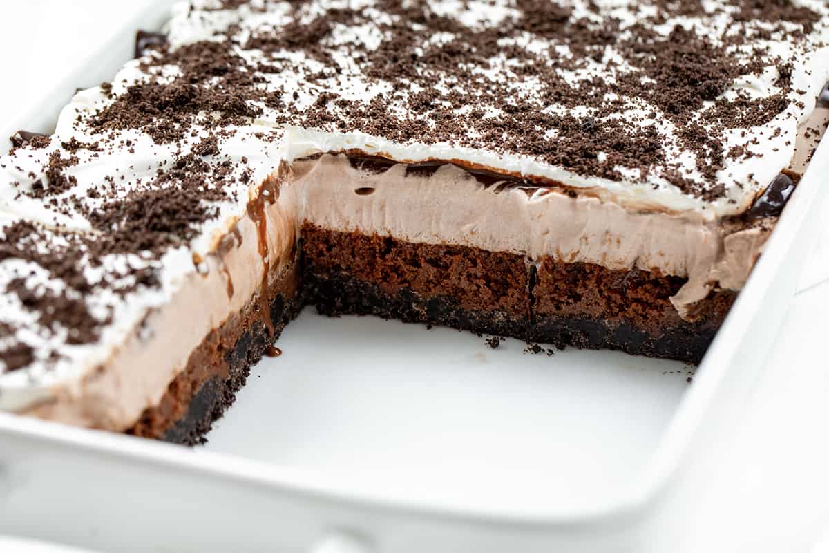 Chocolate Mud Bars are a rich and indulgent layered dessert with an Oreo cookie crust topped with fudgy brownies, chocolate mousse, hot fudge, and whipped cream. It's a chocolate lover's dream dessert that combines different textures and flavors to create a truly lavish treat! Pan of Chocolate Mud Bars on White Counter.