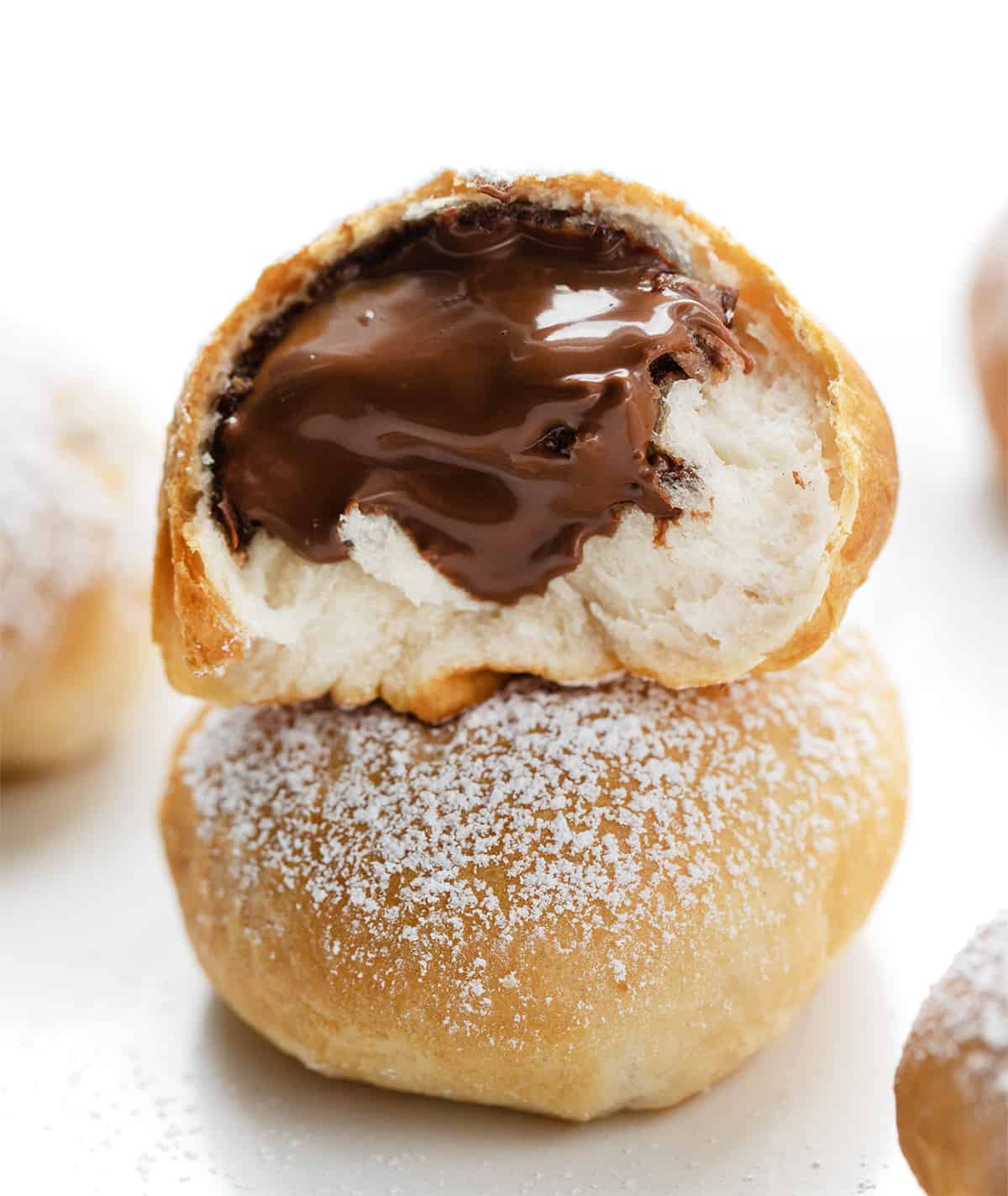 Nutella Bombs are sweet treats made with just four simple ingredients and cooked in an air fryer. They start with a can of refrigerated biscuits that are separated and filled with Nutella. After rolled up into balls, they are cooked to a golden brown. Then, to top it all off, literally, confectioners' sugar is dusted over the tops. Each bite is bursting with Nutella! (I will also let you know how to bake these in the oven. Cut in Half Nutella Bomb Showing Nutella Inside.