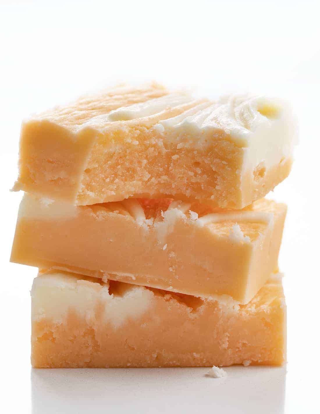 Orange Creamsicle Fudge is a sweet fudge made with just the right amount of orange flavor and white chocolate chips for a soft and smooth treat. Creamsicle, Orange Creamsicle, Creamsicle Fudge, Creamy Fudge, Fudge Recipe, How to Make Fudge, Dessert, recipes, BBQ, cookout dessert, July 4th dessert, i am baker, iambaker Stacked and Bit Into Orange Creamsicle Fudge