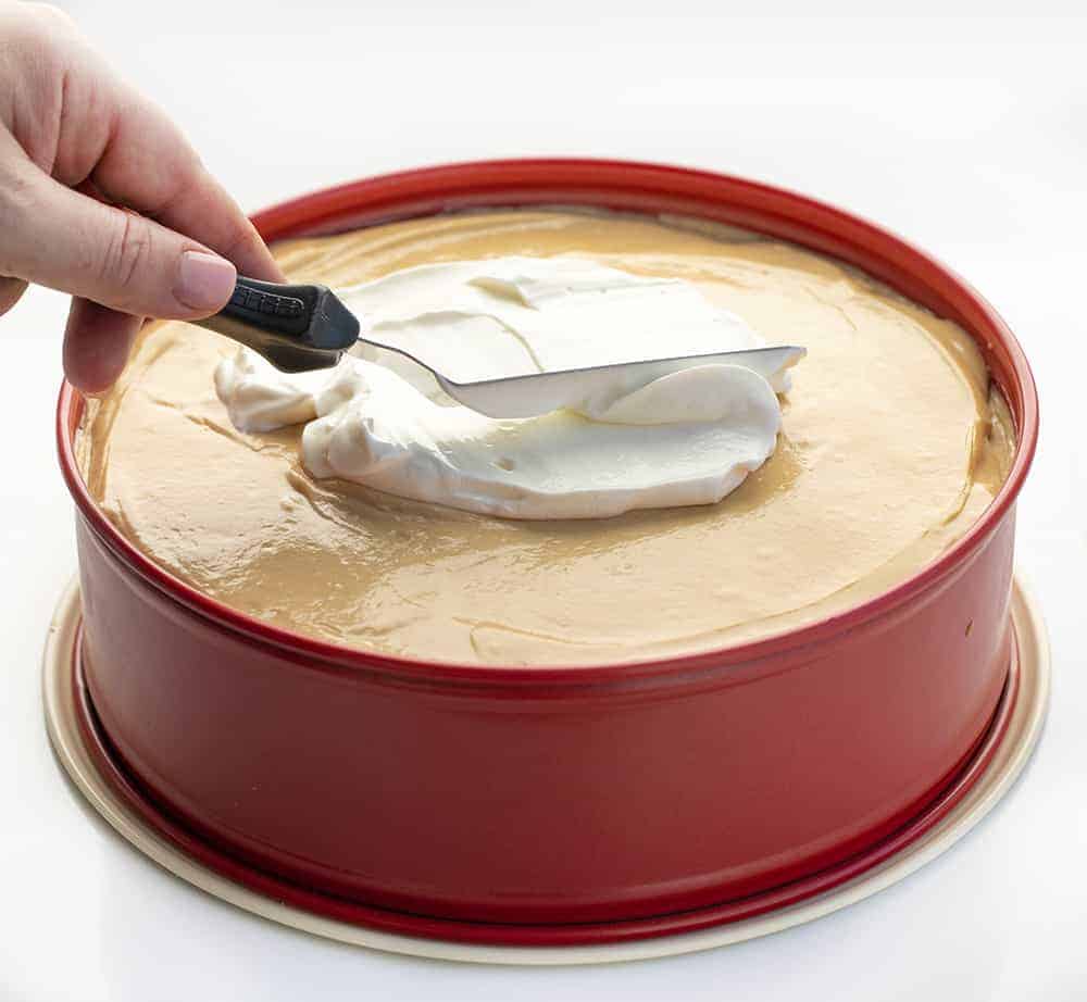 Peanut Butter Cheesecake is a smooth and creamy cheesecake made with peanut butter and a homemade peanut butter cookie crust. Peanut Butter Cheesecake, Decadent Cheesecake, Cheesecake Recipes, Peanut Butter Desserts, Dessert, Triple Peanut Butter Cheesecake, i am baker, iambaker, recipes, Christmas, New Years Eve Spreading Sour Cream on Peanut Butter Cheesecake