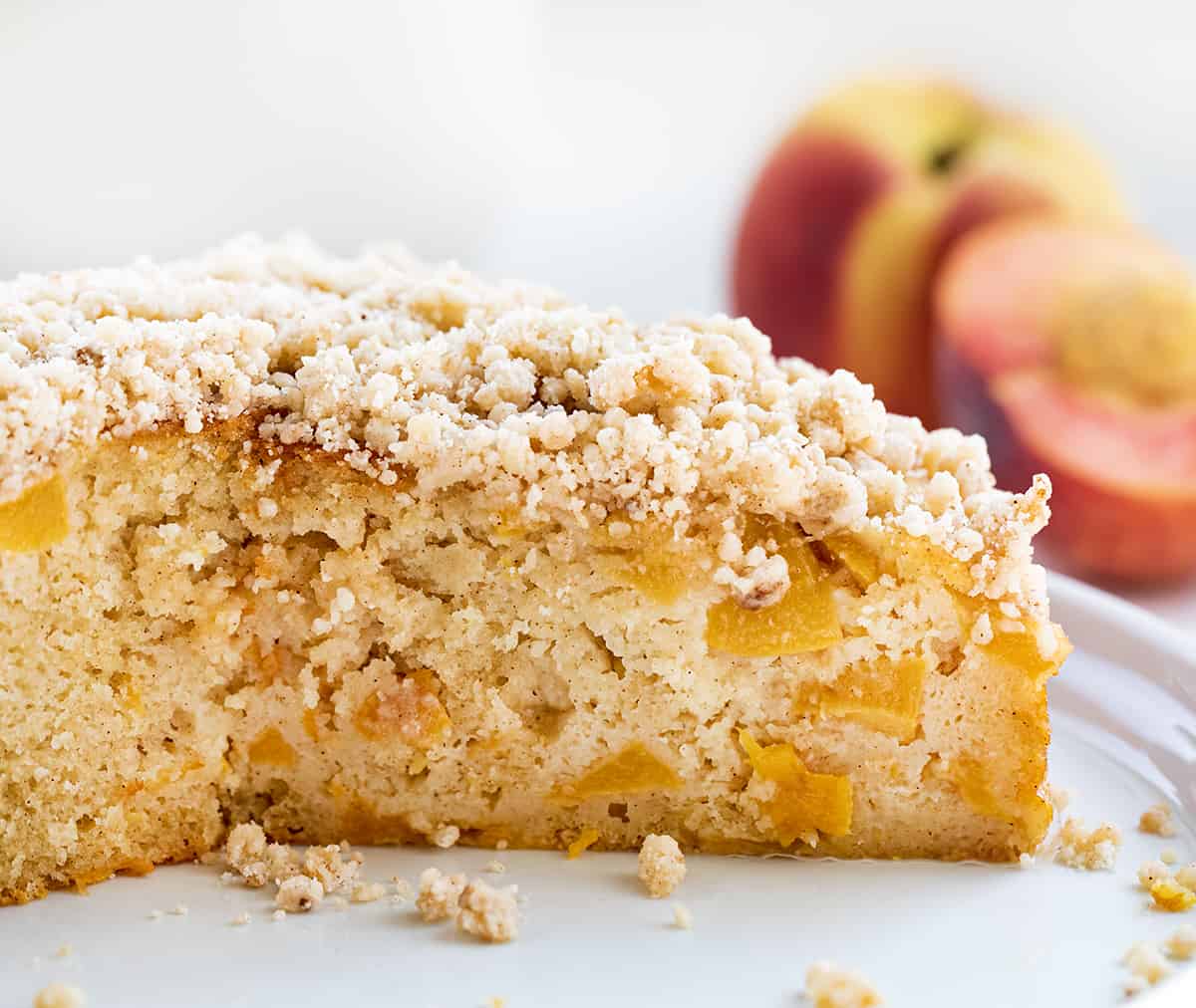 Peach Cake is loaded with peaches, baked to a tender and moist crumb, then drenched with a sweet warm milk mixture and sprinkled with a crumble topping. This is an absolute must-try for anyone who loves peaches or is simply craving a sweet dessert! Cut Into Peach Cake Showing Inside Texture.