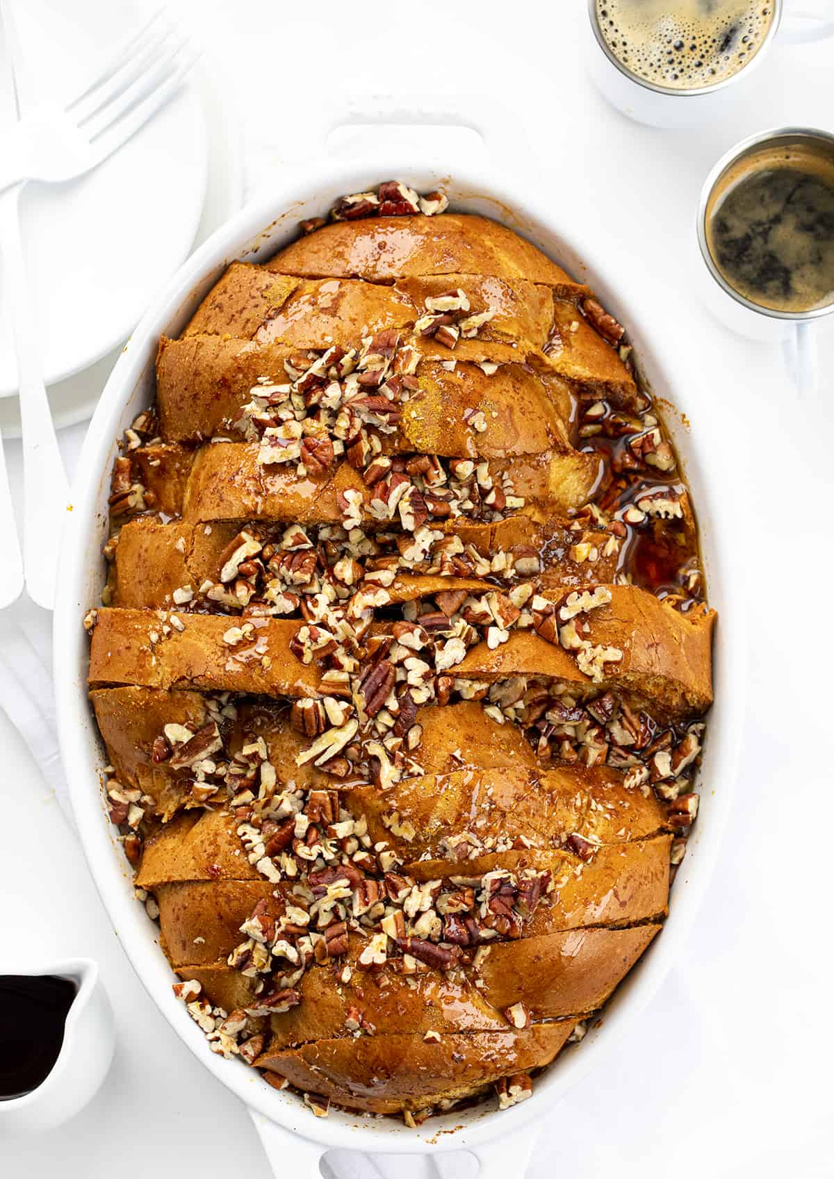 Pumpkin French Toast Casserole is slices of Challah bread dipped into a pumpkin-flavored custard mixture, sprinkled with pecans, and baked for a warm breakfast or brunch. It's a perfect recipe to prepare the night before and get in the oven the next morning! Pumpkin French Toast Casserole in a White Casserole Dish on a Counter with Espresso.
