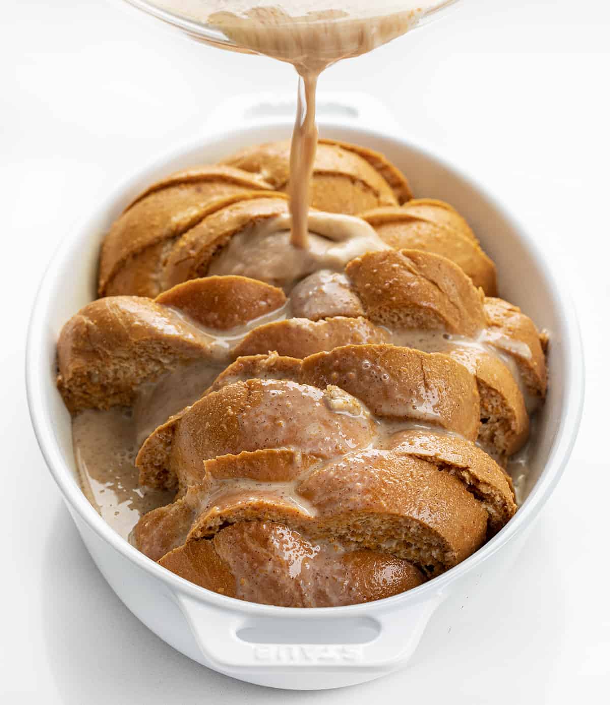 Pumpkin French Toast Casserole is slices of Challah bread dipped into a pumpkin-flavored custard mixture, sprinkled with pecans, and baked for a warm breakfast or brunch. It's a perfect recipe to prepare the night before and get in the oven the next morning! Pouring Egg Mixture Over Bread in Casserole Pan for Pumpkin French Toast Casserole.