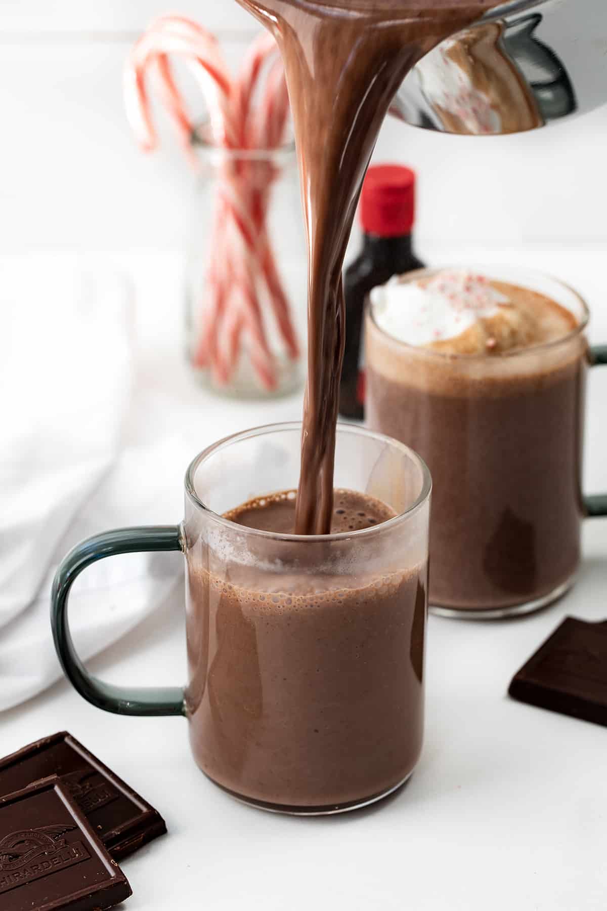 This creamy, smooth, velvety Peppermint Hot Chocolate is a Holiday must have! Just like we have a pumpkin spice season every Autumn, it seems to be peppermint season once we hit the holidays. With candy canes associated with Christmas, that peppermint flavor has been added to everything from cookies, to desserts, to candy, and drinks like this one. And, once you taste this peppermint hot chocolate, you will want to keep the recipe handy for any time you crave a minty chocolate treat. Pouring Peppermint Hot Chocolate into a Glass.