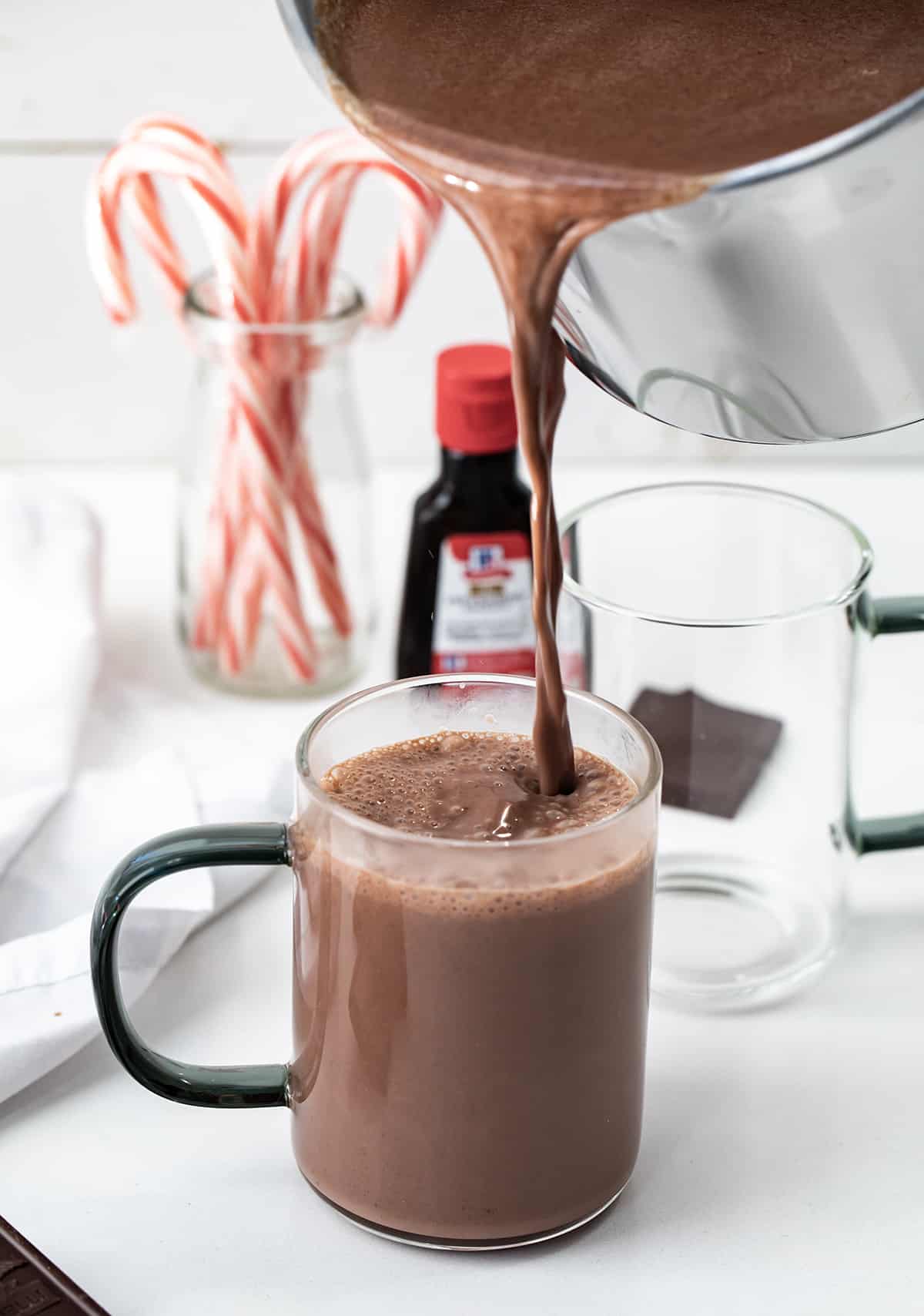 This creamy, smooth, velvety Peppermint Hot Chocolate is a Holiday must have! Just like we have a pumpkin spice season every Autumn, it seems to be peppermint season once we hit the holidays. With candy canes associated with Christmas, that peppermint flavor has been added to everything from cookies, to desserts, to candy, and drinks like this one. And, once you taste this peppermint hot chocolate, you will want to keep the recipe handy for any time you crave a minty chocolate treat. Pouring Peppermint Hot Chocolate into a Glass.
