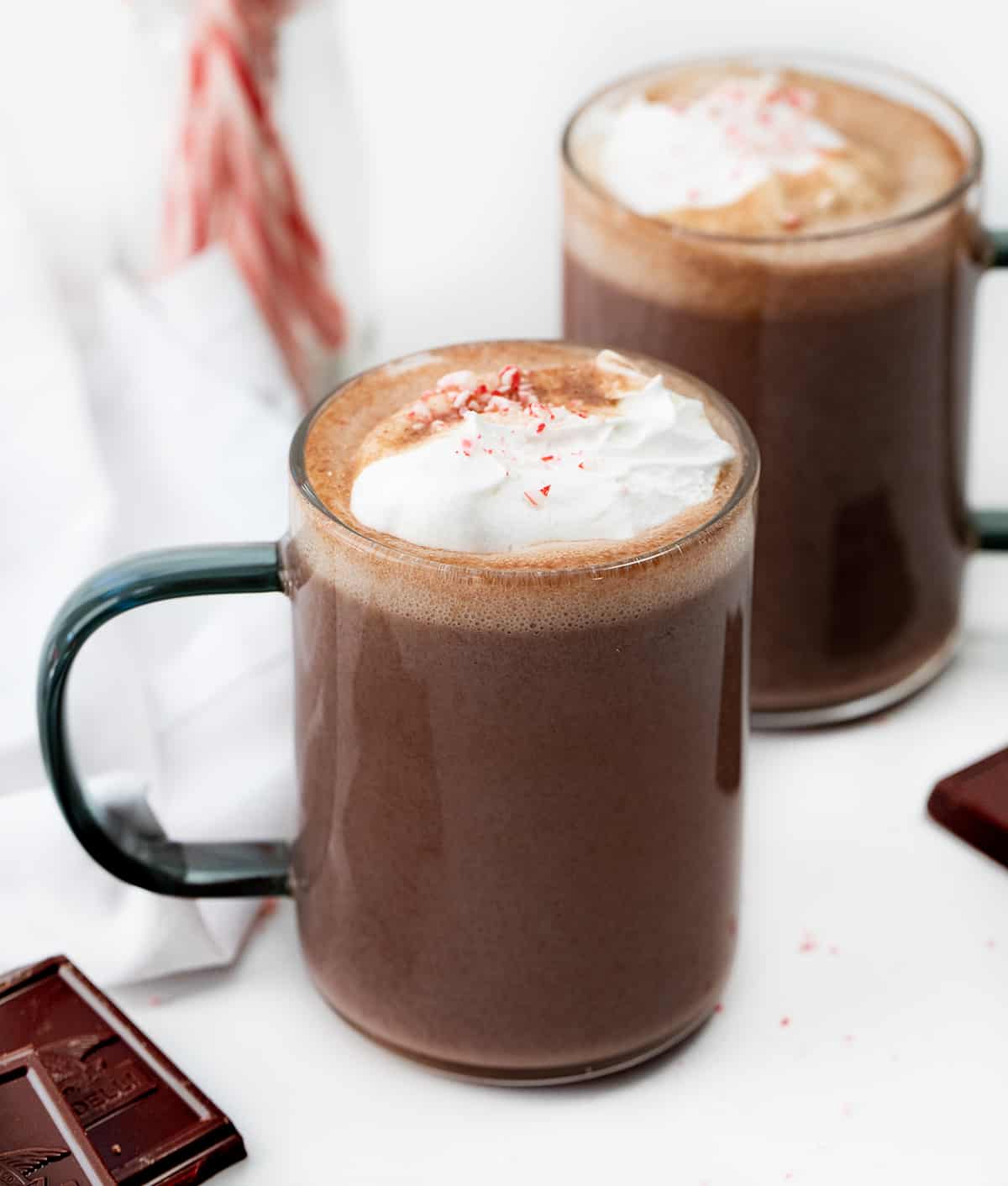 This creamy, smooth, velvety Peppermint Hot Chocolate is a Holiday must have! Just like we have a pumpkin spice season every Autumn, it seems to be peppermint season once we hit the holidays. With candy canes associated with Christmas, that peppermint flavor has been added to everything from cookies, to desserts, to candy, and drinks like this one. And, once you taste this peppermint hot chocolate, you will want to keep the recipe handy for any time you crave a minty chocolate treat. Glasses of Peppermint Hot Chocolate on a Counter.