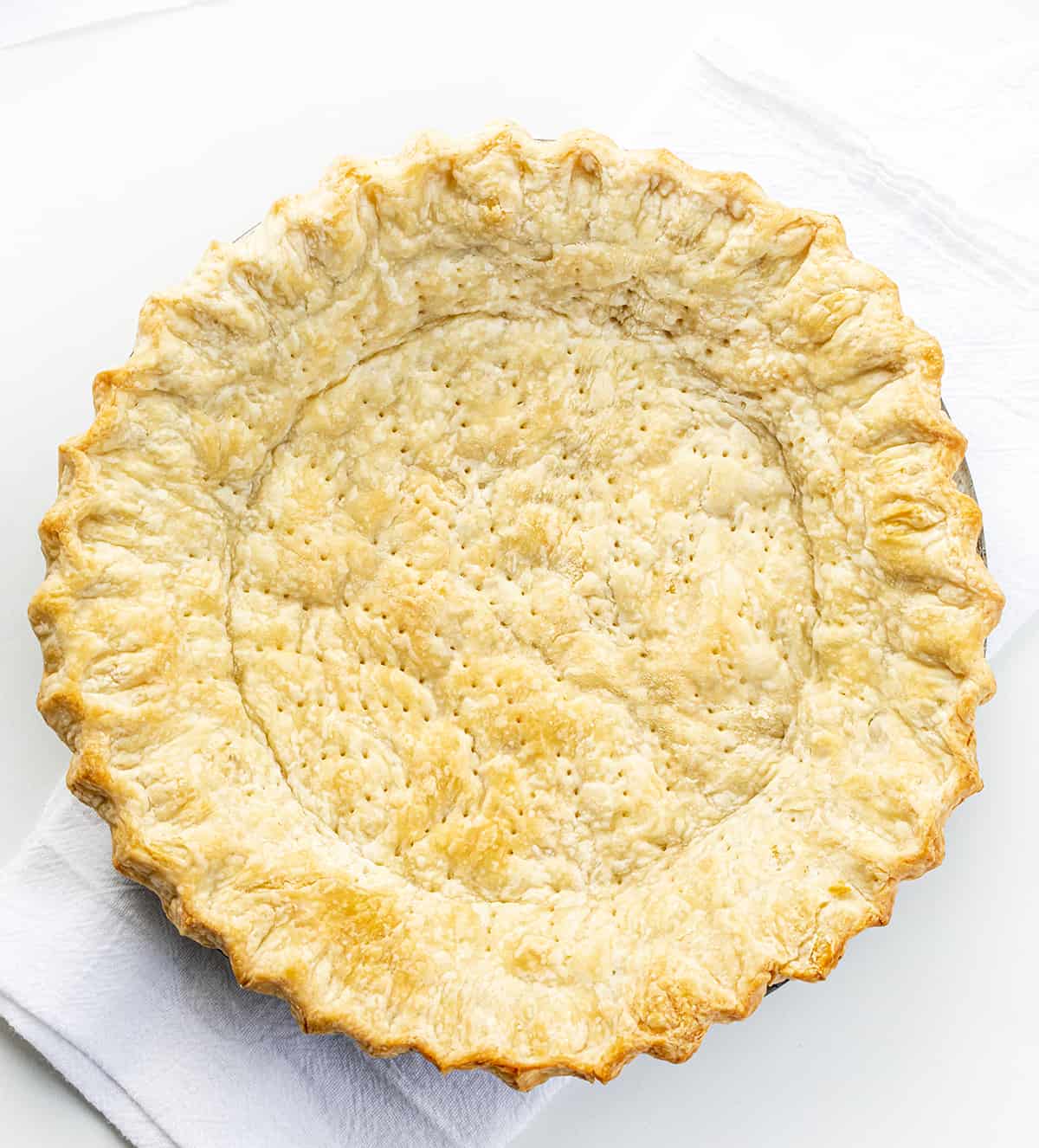 Do you want the best no-fail ALL BUTTER Pie crust? Professional bakers agree, this one tastes the best! A Baked All Butter Pie Crust in a Pan with No Filling on a White Counter.