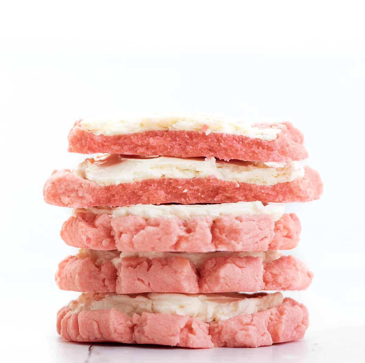 Stack of Pink Velvet Sugar Cookies with Easy Swiss Meringue Frosting with the Top Cookies Broken in Half.