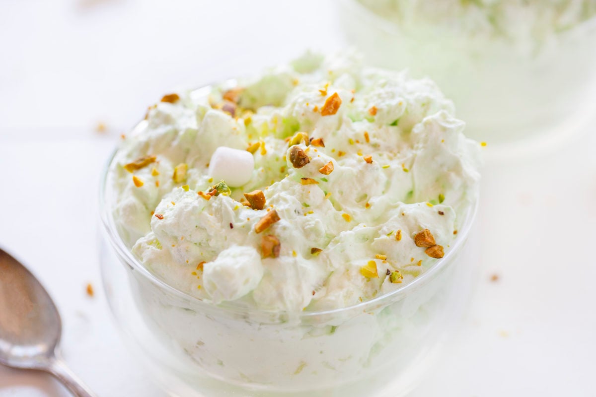 The best no-bake desserts to get your sweet tooth through the summer! no bake, no bake desserts, desserts, recipes, cheesecake, cookies, bars, cake, pudding, mousse, puppy chow, muddie buddies, rice krispy bars, dessert, memorial day dessert, labor day desserts, i am baker, iambaker Pistachio Fluff or Watergate Salad on a Bowl with Chopped Pistachio on Top.
