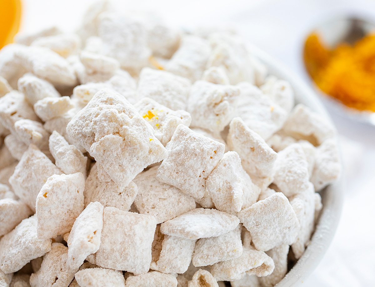 The best no-bake desserts to get your sweet tooth through the summer! no bake, no bake desserts, desserts, recipes, cheesecake, cookies, bars, cake, pudding, mousse, puppy chow, muddie buddies, rice krispy bars, dessert, memorial day dessert, labor day desserts, i am baker, iambaker Orange Creamsicle Puppy Chow on White Bowl.