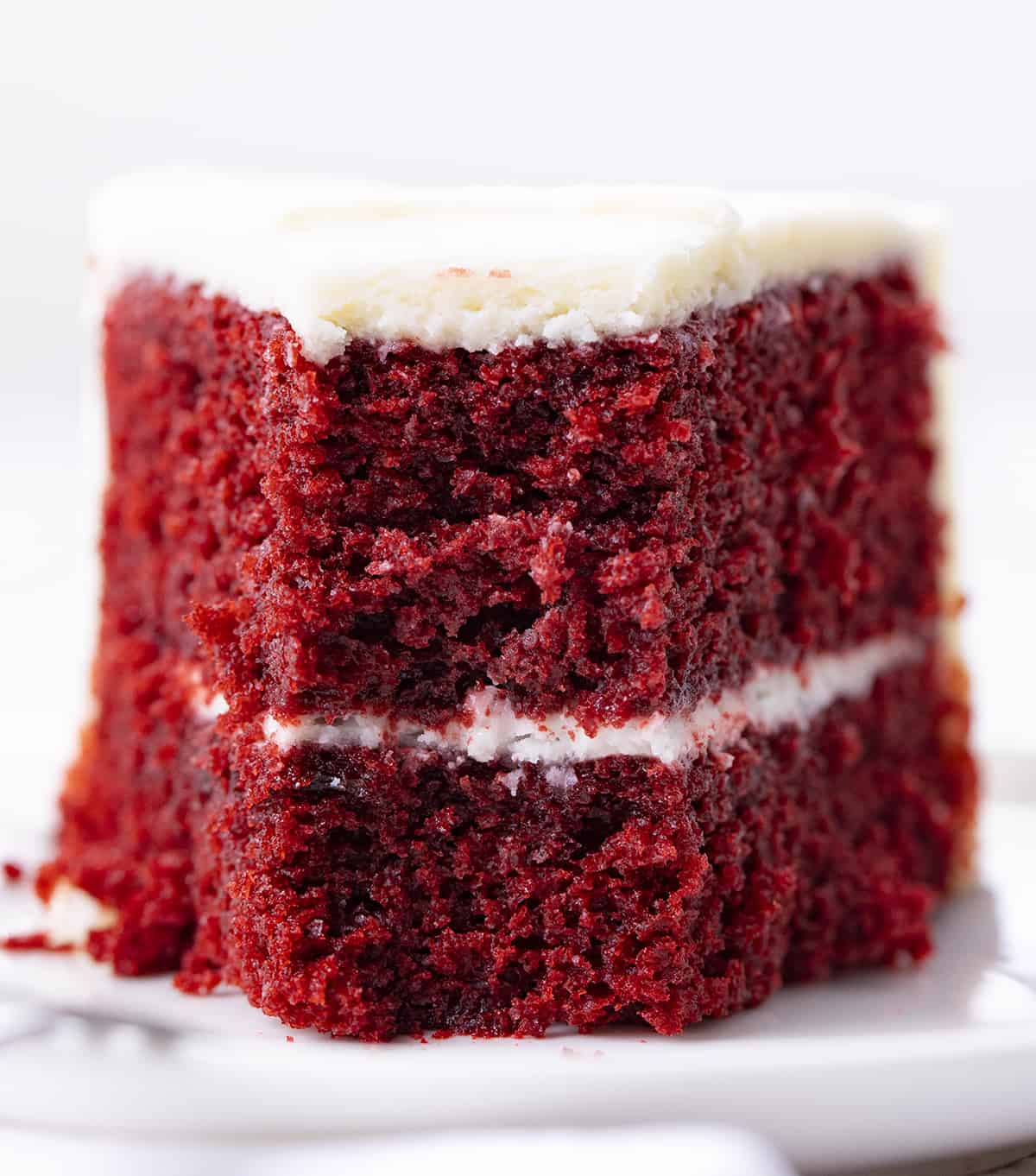 The perfect Red Velvet cake has a rich, deep flavor and a color to match! Then paired with the perfect cream cheese frosting, this just might be the perfect cake! Piece of red velvet cake on a plate with a bite removed.