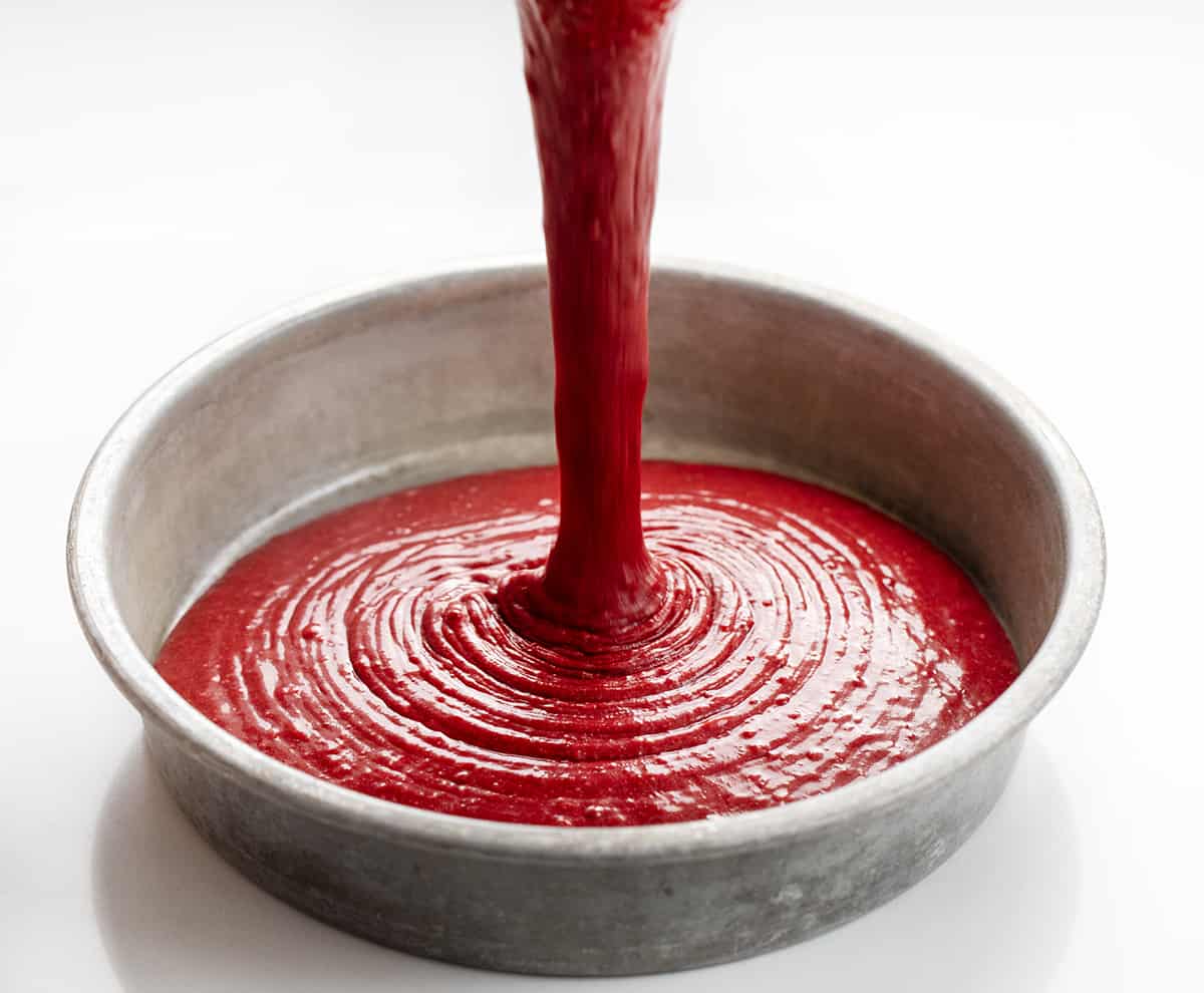 The perfect Red Velvet cake has a rich, deep flavor and a color to match! Then paired with the perfect cream cheese frosting, this just might be the perfect cake! Pouring red velvet cake batter into round baking pan.