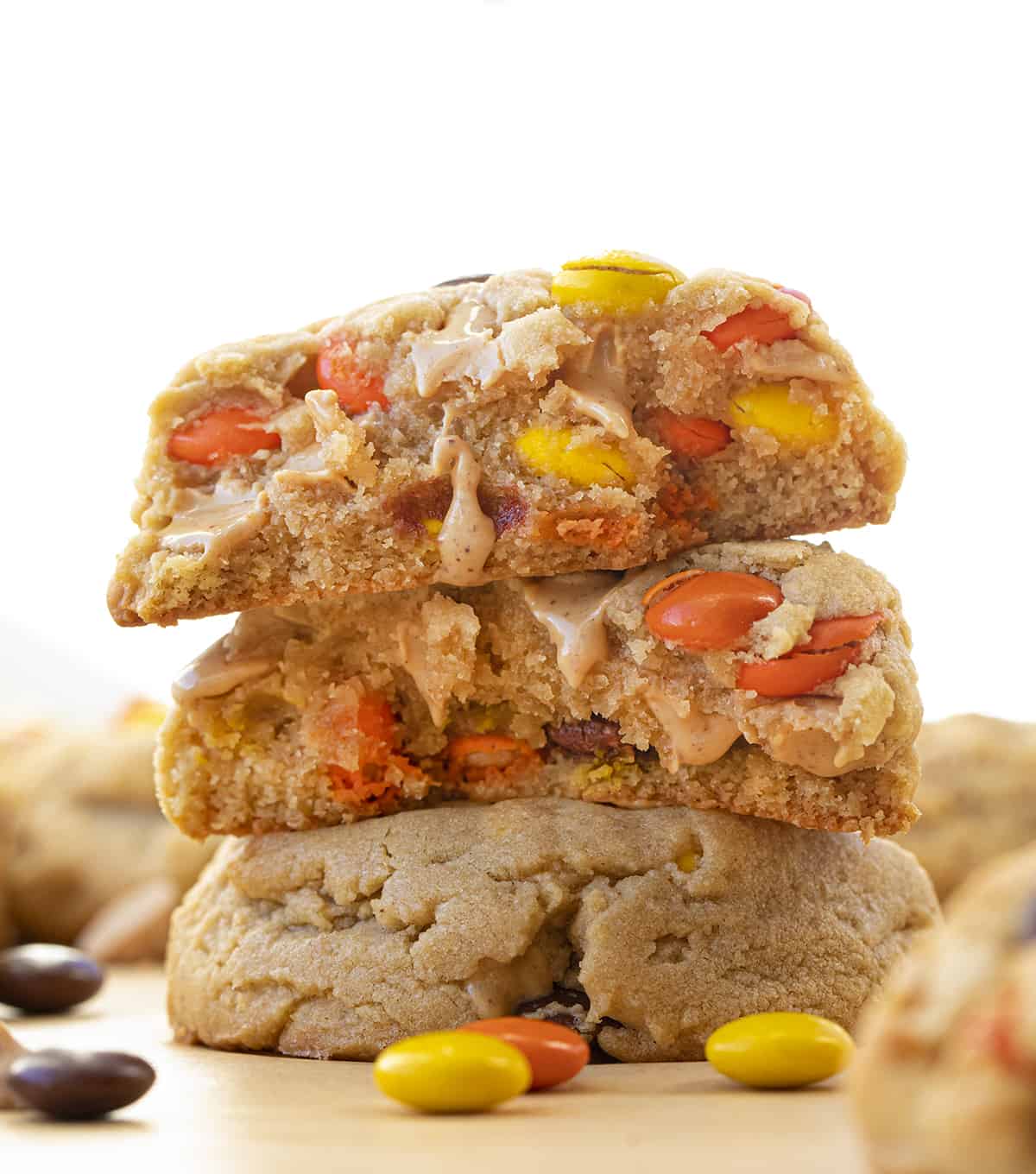 These Reese’s Pieces Peanut Butter Cookies are a cookie lovers dream come true! As you can probably tell, I did not skimp on the peanut butter flavor in these cookies. They are the ultimate peanut butter cookie. There is peanut butter in the dough, as well as peanut butter chips, and two whole cups of Reese’s pieces! These cookies are so gooey in the center and perfectly crisp on the outside! (Perfect for a Christmas charcuterie board or Cookie Exchange!) Stacked Reese's Pieces Peanut Butter Cookies and Top Cookie Broken in Half Showing Inside.