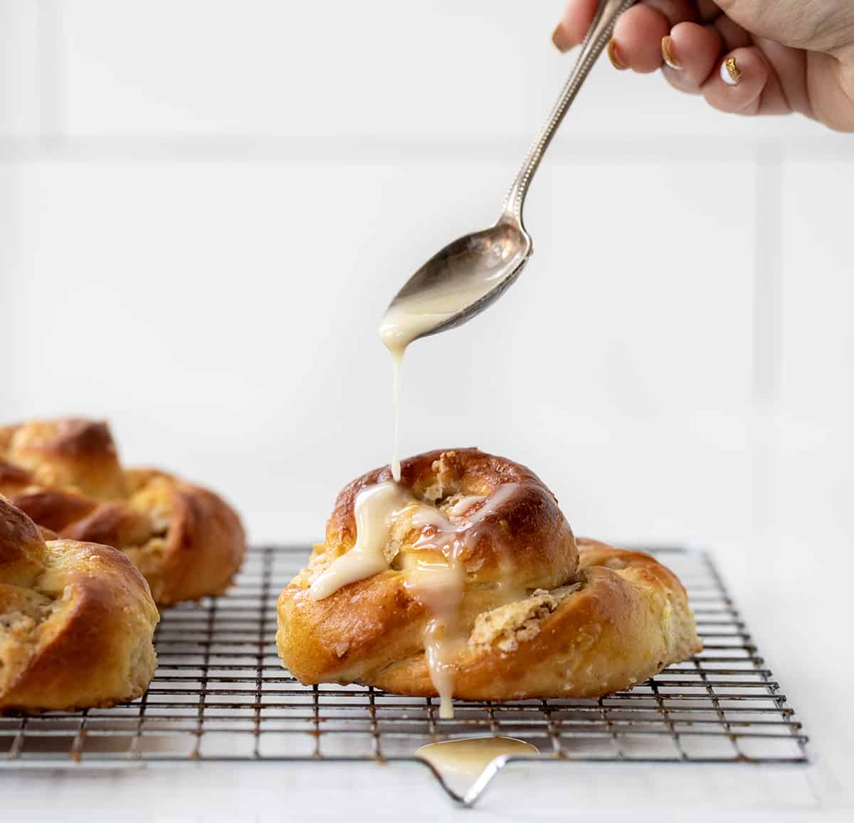 A Ring A Ling Pastry is a delicious and flavorful treat that combines a sweet dough with a nutty filling and tangy orange glaze. It's a copycat recipe from the 1955 Pillsbury Bake-Off winning recipe by Bertha Jorgensen. The spiral design is easy to do and gives you all the flavors of the pastry in every bite! Adding Glaze to Ring A Ling Pastry on a Cooling Rack.