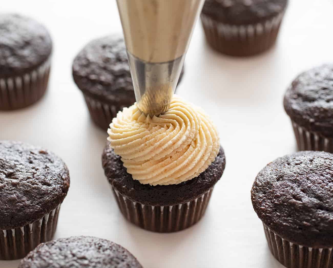 Chocolate Cupcakes with Salted Caramel Buttercream take my Ultimate Chocolate Cupcakes to a whole new salted caramel level! Chocolate Cupcakes, Salted Caramel Buttercream, caramel buttercream, how to make caramel buttercream, chocolate cupcakes, easy chocolate cupcakes, new years eve cupcakes, elegant cupcakes, salted caramel, i am baker Piping Frosting onto Chocolate Cupcake