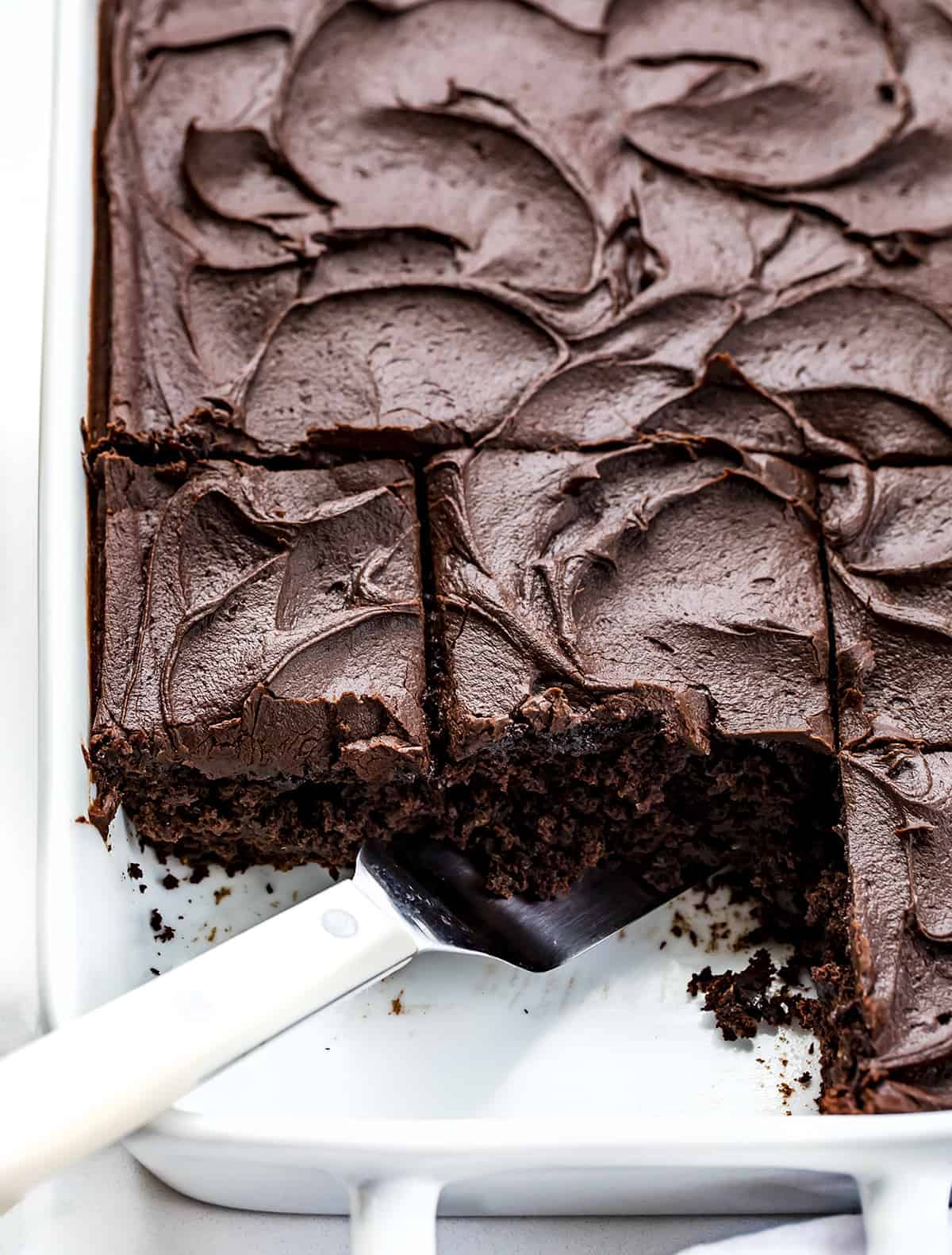 Chocolate Sauerkraut Cake is a soft and moist chocolate cake topped with a thick and creamy chocolate frosting. Chocolate Cake, Sauerkraut Cake, Chocolate Sauerkraut Cake, Vintage Cake, Old Fashioned Cake, Grandma's Chocolate Cake, Baking, Dessert, Chocolate Frosting, recipes, i am baker, iambaker Pan of Chocolate Sauerkraut Cake with Two Pieces Missing and the Spatula in the Pan.