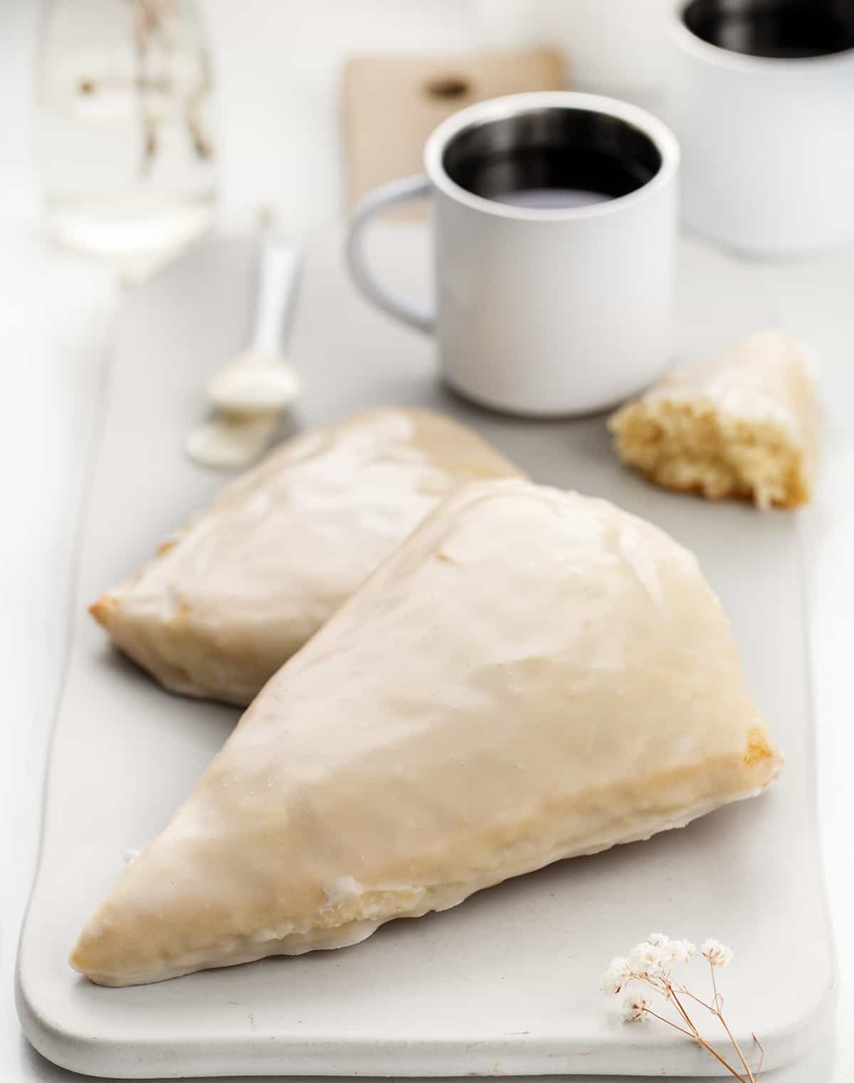 My sconut recipe will give you the perfect texture of a scone with the irresistible flavor of a doughnut, all in one bite! Plus, the best part? They're baked in the oven, not fried, making them a healthier option. Whether you can't decide between a scone or a doughnut or simply love both, this recipe is a must-try for all scone and doughnut lovers! Plated Sconuts with Cups of Espresso and Flowers.