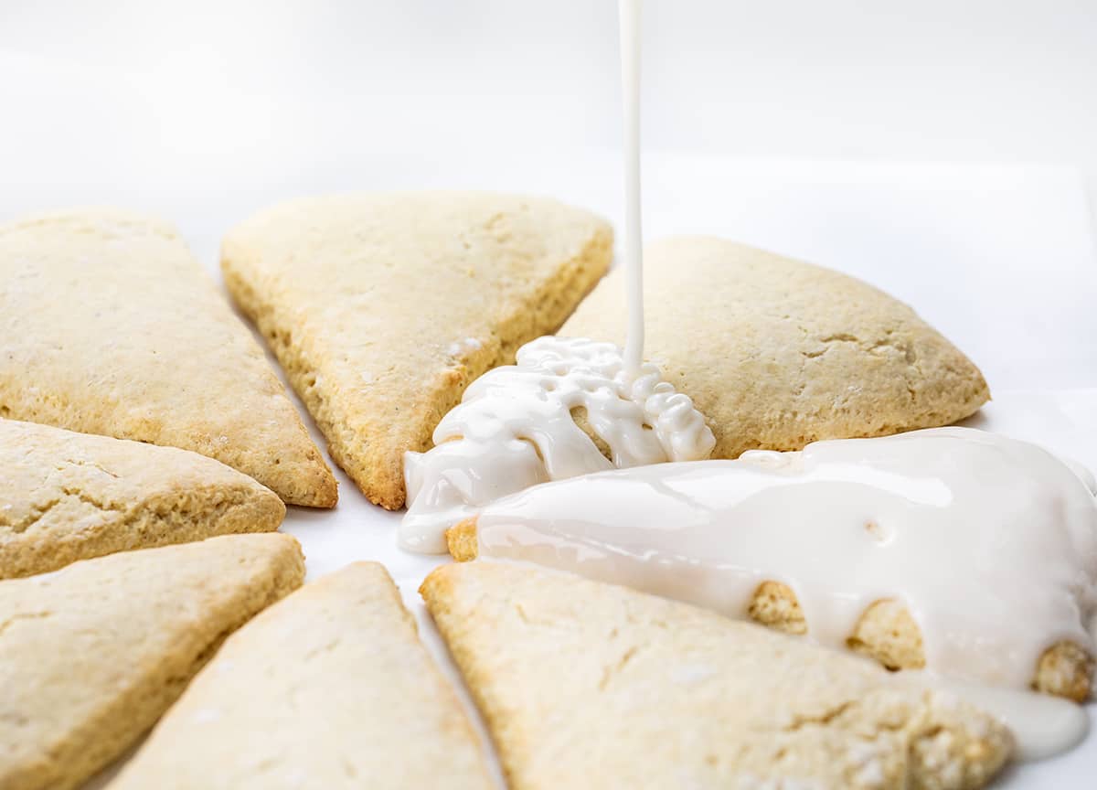 My sconut recipe will give you the perfect texture of a scone with the irresistible flavor of a doughnut, all in one bite! Plus, the best part? They're baked in the oven, not fried, making them a healthier option. Whether you can't decide between a scone or a doughnut or simply love both, this recipe is a must-try for all scone and doughnut lovers! Drizzling Glaze over Freshly Baked Sconuts.