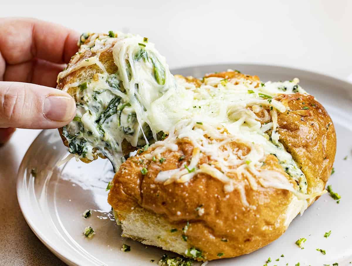 Take your appetizer to the next level with this Spinach Artichoke Dip Pull-Apart Bread! Spinach Artichoke Bread, Garlic Spinach Bread, Pull Apart Bread, Appetizer, How to Make Individual Spinach Artichoke Breads, Cheesy Pull Apart Bread, recipes, i am baker, iambaker Hand Pulling Apart Spinach Artichoke Bread