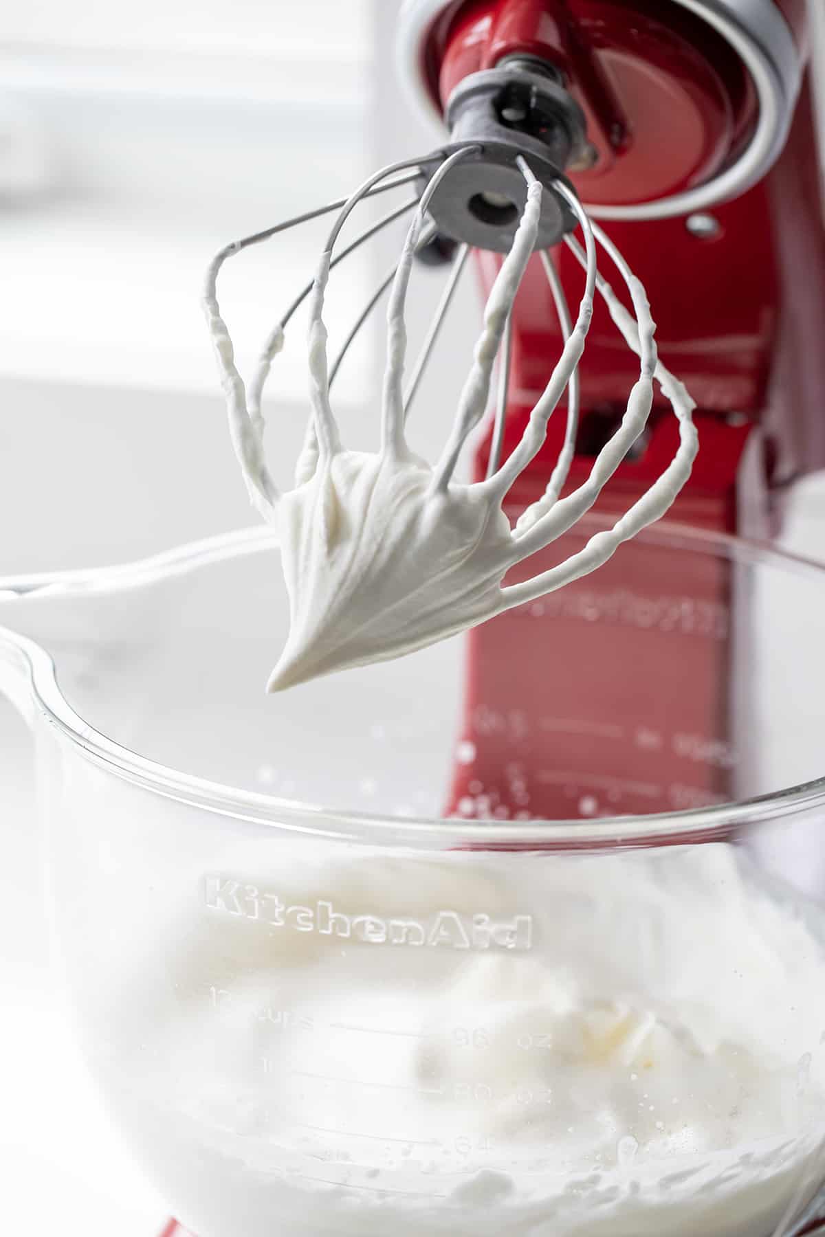 Stabilized Whipped Cream is a versatile ingredient that can be used in many types of desserts from frosting to filling to a topping. It tastes like homemade whipped cream (delicious!), it holds its shape beautifully, and it lasts for days! This just might be my new favorite addition to all my favorite desserts Mixer with whisk attachment with whipped cream on it, showing the stiff peaks.