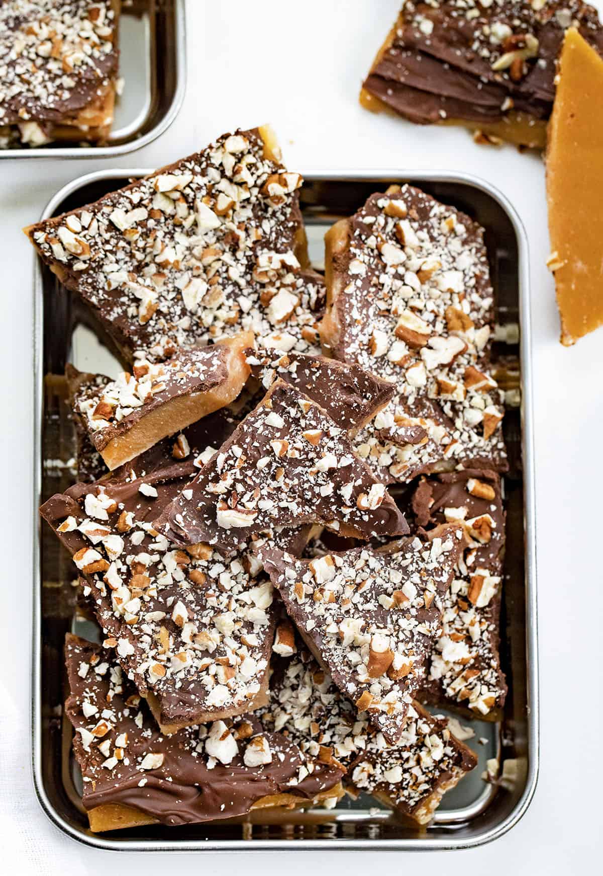 Learn how to make the BEST English Toffee that looks and tastes amazing! Rich buttery toffee covered with milk chocolate and chopped pecans. Just 4 ingredients! English toffee is the perfect holiday candy treat for parties and Christmas gifts. Trays of Homemade English Toffee broken into Pieces.