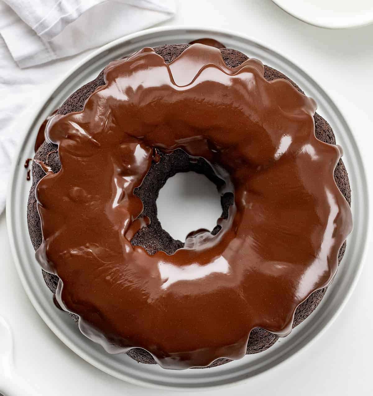Death By Chocolate Bundt Cake is a chocolate cake with a chocolate cream cheese filling baked in a bundt pan and then topped with chocolate butter ganache. Chocolate Bundt, Triple Chocolate Bundt, Chocolate Cheesecake Chocolate Bundt, Death by Chocolate Bundt Cake, Butter Chocolate Ganache, How to Make Ganache with Just Butter, Chocolate Cream Cheese, Dessert, Baking, Decadent Dessert, Holiday Dessert, Christmas Dessert, New Years Dessert, i am baker, iambaker OVerhead image of Death by Chocolate Fudge Bundt Cake on White Plate