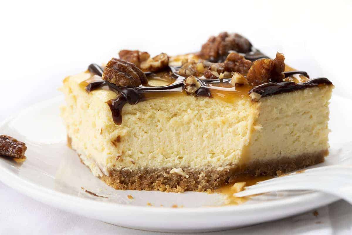Turtle Cheesecake Bars are creamy dessert bars with a graham cracker crust and cheesecake filling, topped with caramel, candied pecans, and hot fudge. Turtle Cheesecake, Cheesecake Bars, Turtle Cheesecake Bars, Dessert, Cheesecake, Best Cheesecake Recipe, i am baker, iambaker, recipes, baking Turtle Cheesecake Bar with Bite Removed