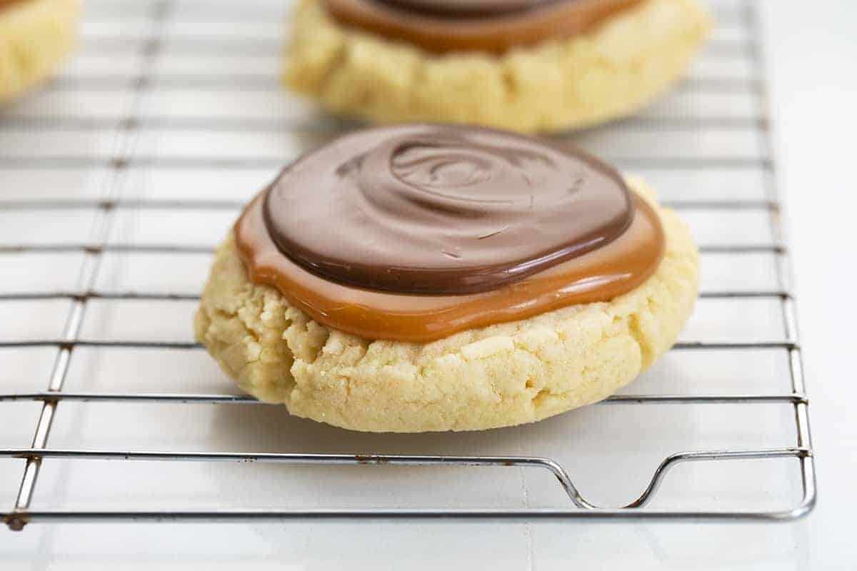 Twix Cookies are large, soft butter cookies topped with caramel sauce and melted milk chocolate. These cookies are like eating a Twix candy bar... but in cookie form! The super-soft cookies are topped with "homemade" caramel and milk chocolate, just like the famous candy bar. Baking, Cookies, Cookie Recipes, Dessert, Caramel Cookies, Caramel Recipe, Milk Chocolate, Kid Approved Snacks, i am baker, iambaker Twix Cookie on a Cooling Rack