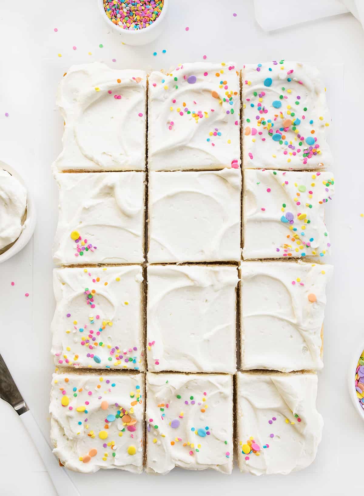 Vanilla Delight Cake (or white cake) is a moist, delicate, and flavorful white sheet cake that is delicious on its own or perfect for your favorite frostings and toppings. It is definitely delightful to snack on, enjoy as a dessert, or share at your next celebration or party! Whole Vanilla-Delight Cake or White Cake on a White Counter with Pastel Sprinkles and Cut Into Pieces.