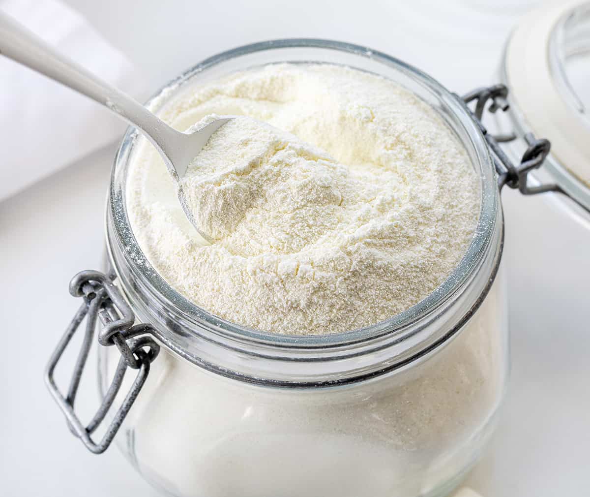 This Big Batch (it makes 20+ cups) of White Hot Chocolate Mix is my new favorite way to enjoy cocoa! As soon as you see how easy it is to make, you will never reach for the packets at the store. It can be added to hot water, hot milk, or even to your cup of coffee. Crockpot Hot Cocoa directions are in the post, which would make it perfect for a Christmas Party, New years Even drink, a mocktail, or a cocktail if you add liquor! And, better yet, it will last up to a year when stored properly. Container with white chocolate hot cocoa mix in it with a spoon.