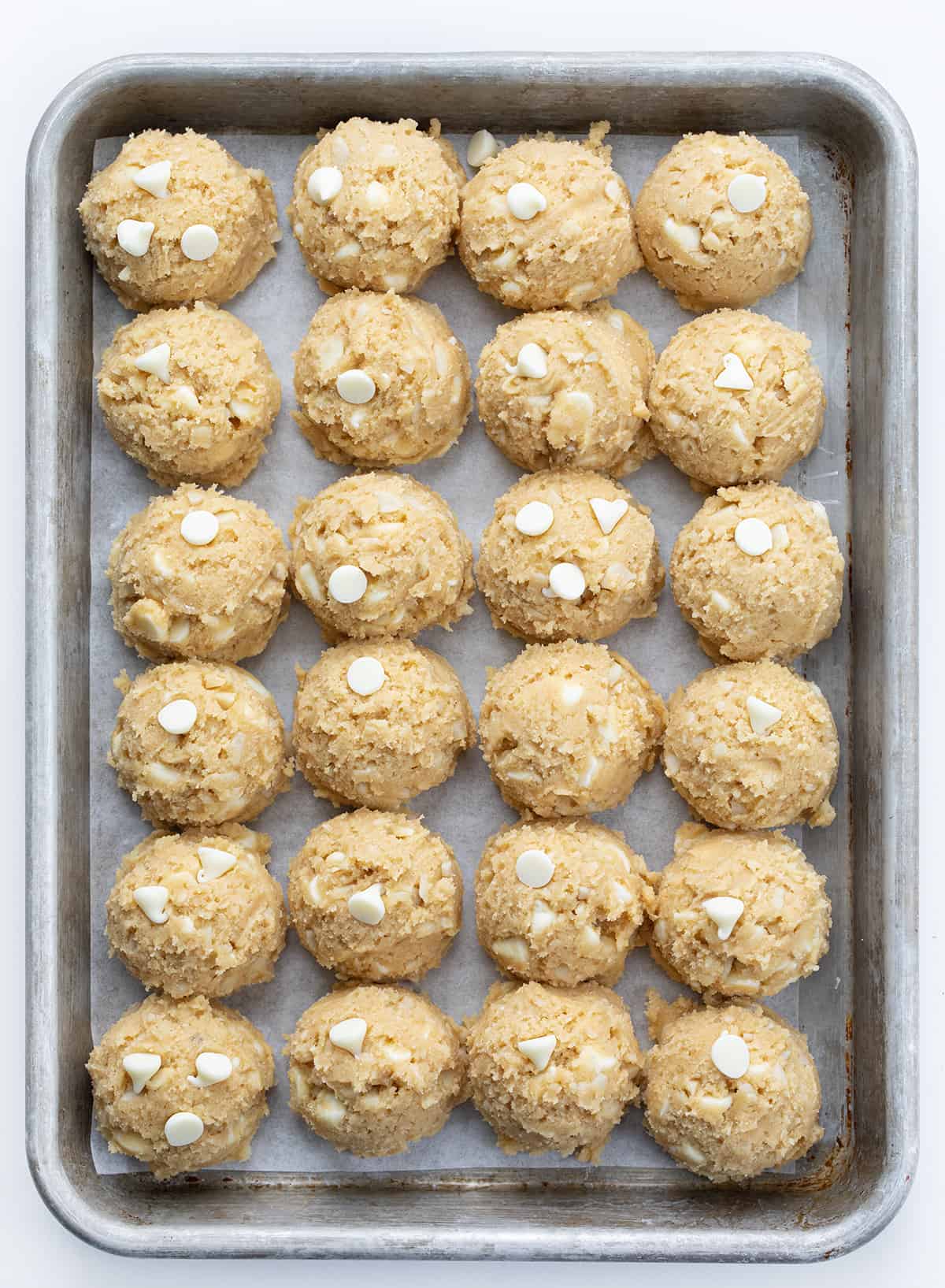 White Chocolate Macadamia Nut Cookies have the rich, buttery flavor of macadamia nuts and the sweet creaminess of white chocolate. These soft, chewy cookies are loaded with white chocolate chips and chopped macadamia nuts for the perfect balance of flavors, great for any occasion! Raw White Chocolate Macadamia Nut Cookie Batter in Scoops on a Baking Sheet.
